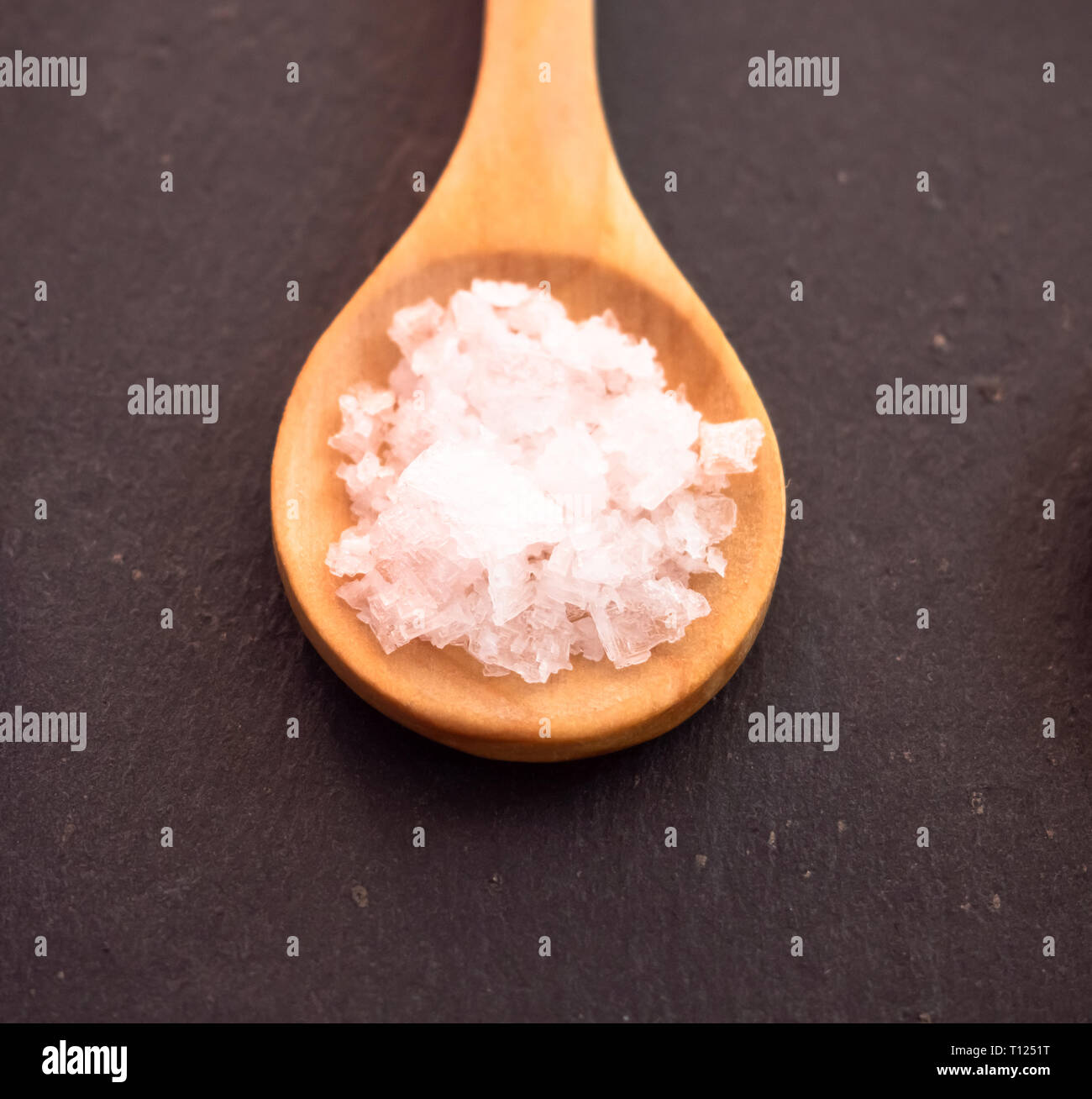 Löffel aus Holz mit Salz Blume Flocken auf einer Schiefertafel Platte Stockfoto