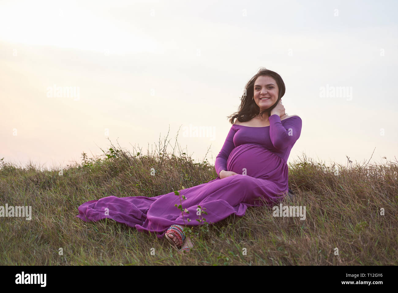 Glücklich lächelnde schwangere Frau sitzen auf Gras Stockfoto