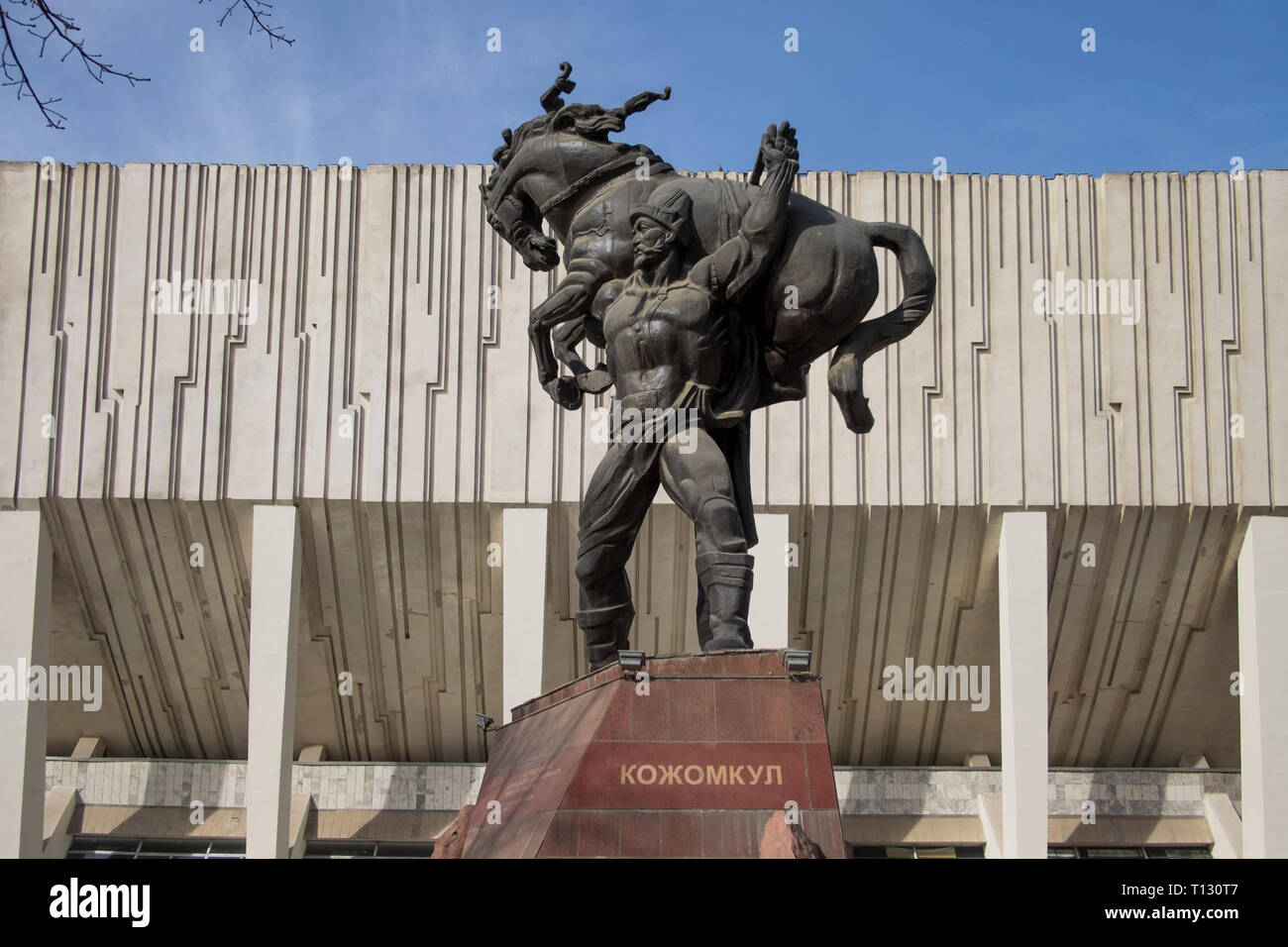 Die Sports Palace Gebäude mit der Krieger legende Kojomkul Skulptur vor der Tür. Das Gebäude ist ein Beispiel für die kommunistische, Sowjetische brutalist Architectur Stockfoto