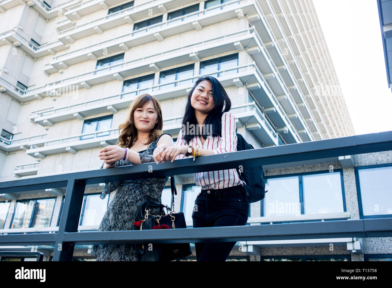 Zwei junge Studentinnen stehen außerhalb ihrer Hochschule modernen Gebäuden auf einem städtischen Campus Stockfoto