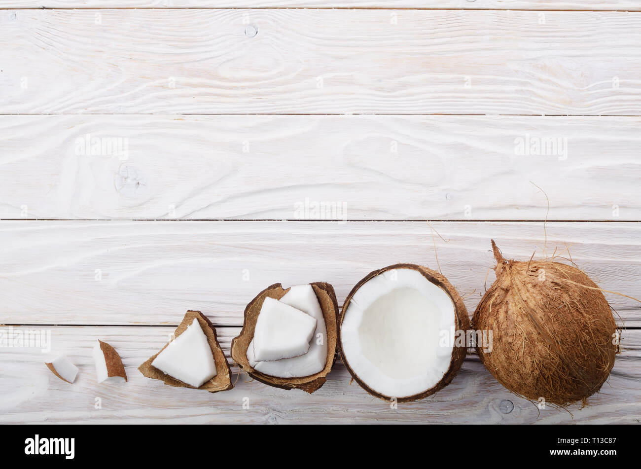 Flach Hintergrund der Kokosnuss, Kokosnussschalen und Fleischstücke auf weissem Holztisch Stockfoto
