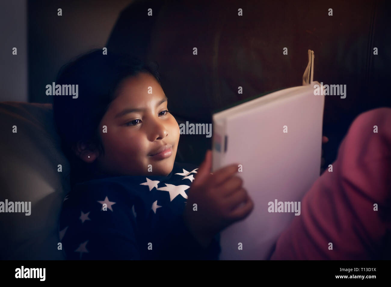 Indische Mädchen tragen Schlafanzug mit Sternen, während eine Geschichte Buch bei Nacht lesen und lächelnd. Stockfoto