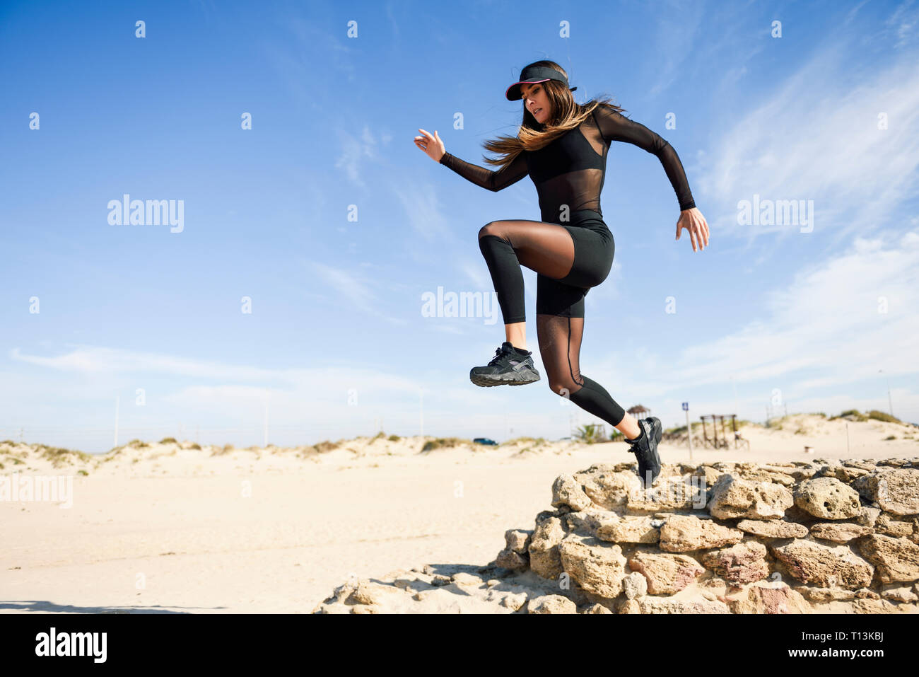 Sportliche Frau Springen von der Mauer aus Stein am Strand Stockfoto