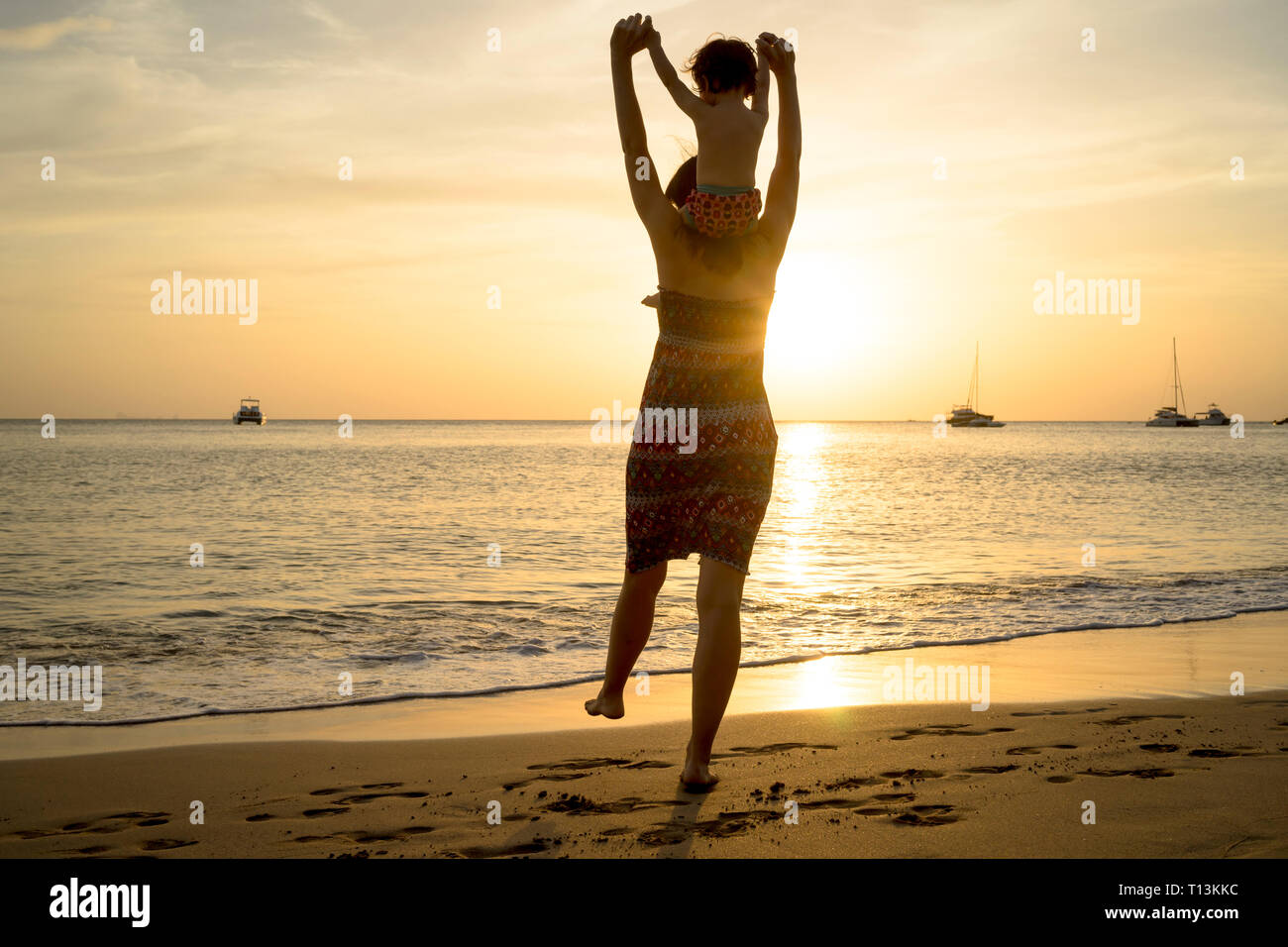 Thailand, Koh Lanta zurück Blick auf Mutter mit Baby Mädchen auf ihren Schultern am Strand bei Sonnenuntergang Stockfoto