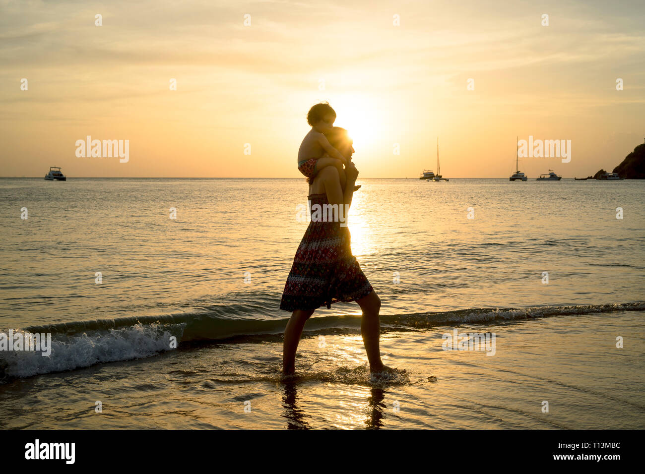 Thailand, Koh Lanta Silhouette der Mutter mit Baby Mädchen auf ihren Schultern am Strand bei Sonnenuntergang Stockfoto