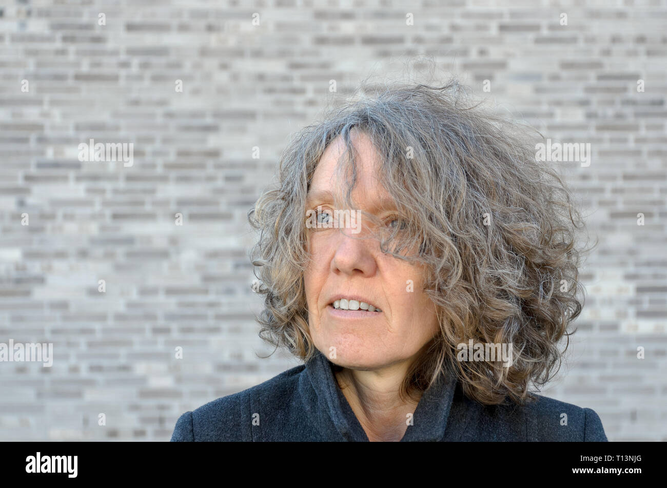 Reifen serios Frau mit Curly zerzaustem Haar auf die Seite, wie Sie sich vor einer grauen Wand mit Kopie Raum Posen Stockfoto