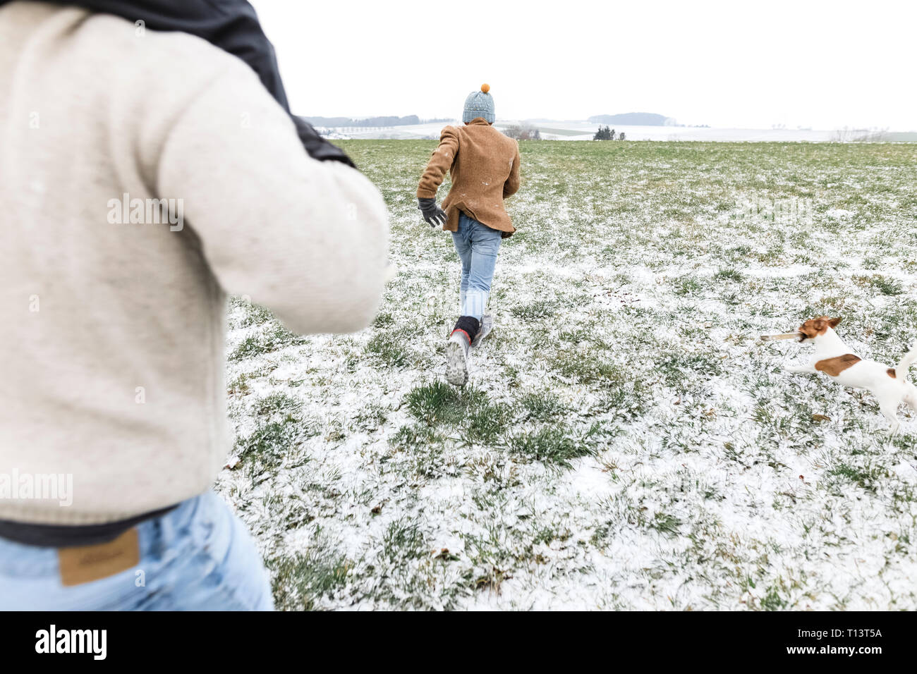 Vater, Sohn und Hund läuft auf verschneiten Feld im Winter Stockfoto