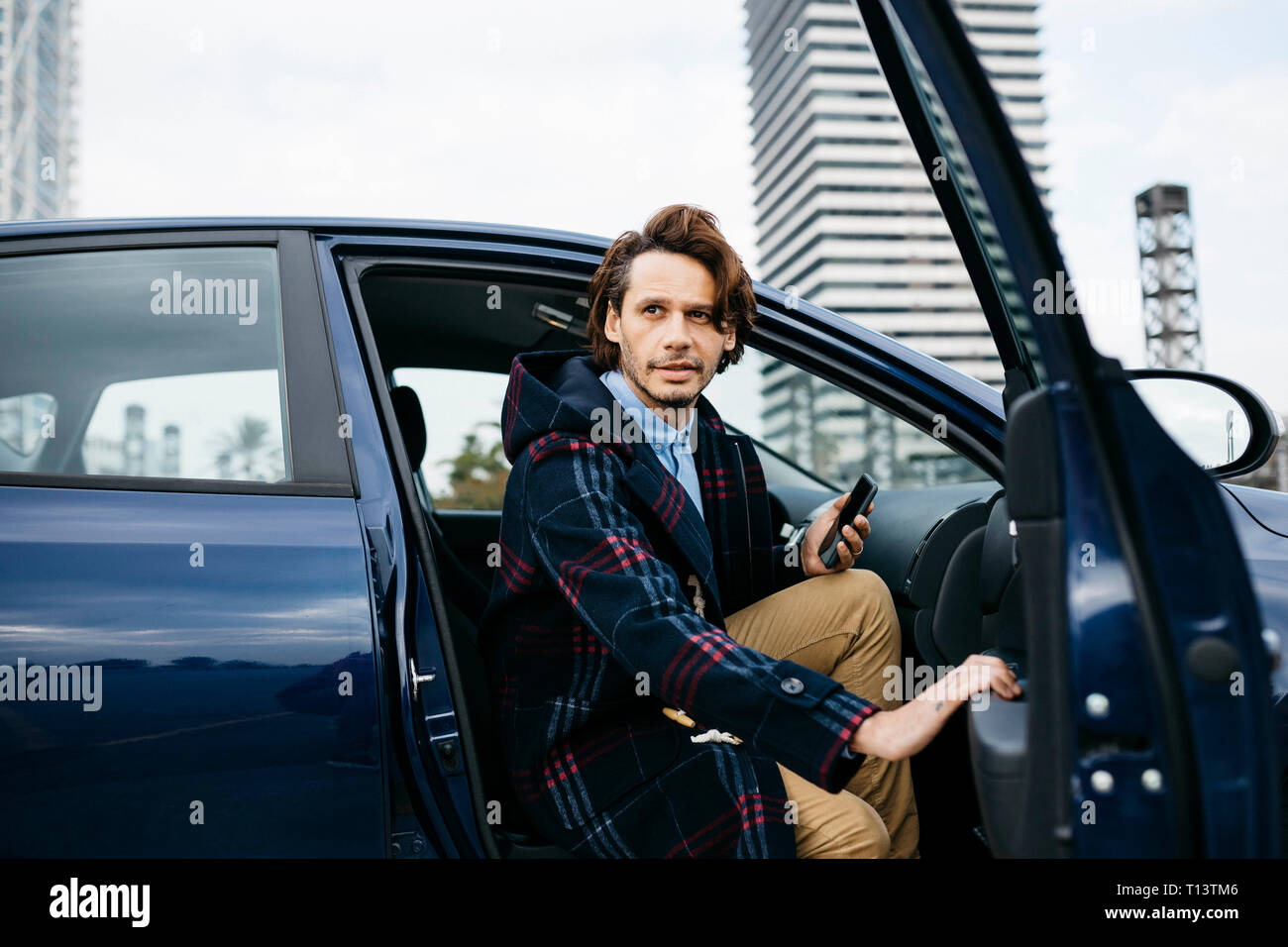 Spanien, Barcelona, mann Aussteigen aus dem Auto mit Handy in der Hand Stockfoto