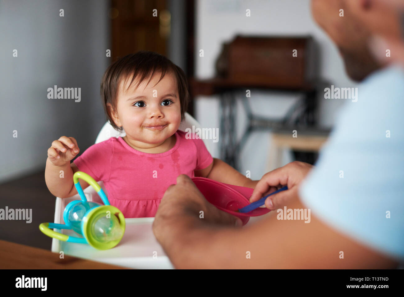Vater feeding Baby Mädchen in hoher Stuhl zu Hause sitzen Stockfoto