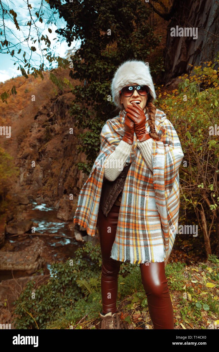 Glückliche junge Reisende Frau in Poncho und Sonnenbrille im Freien Erwärmung der Hände. Stockfoto
