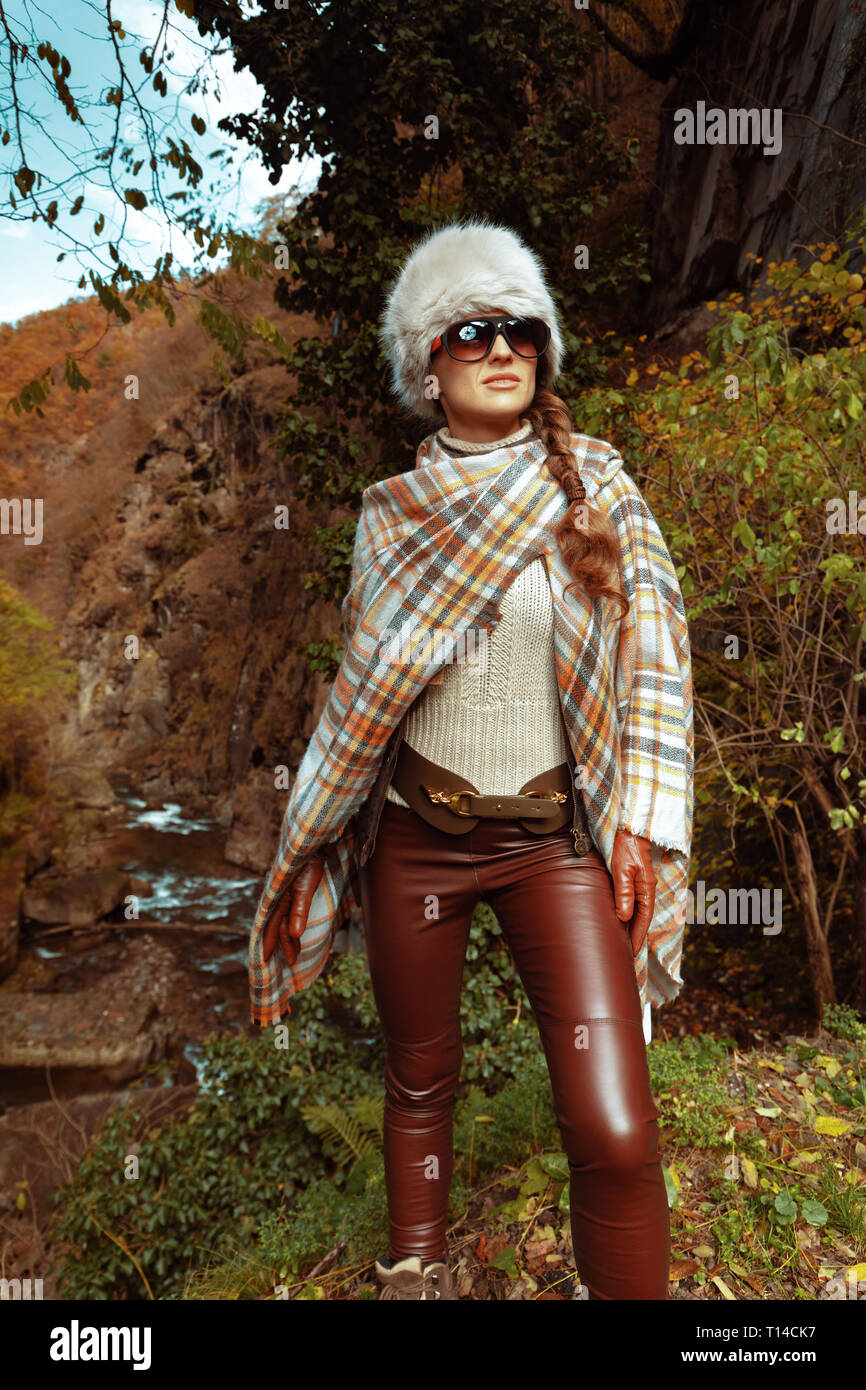 Moderne reisende Frau in Poncho und Sonnenbrille im Wald in die Ferne schauen und. Stockfoto