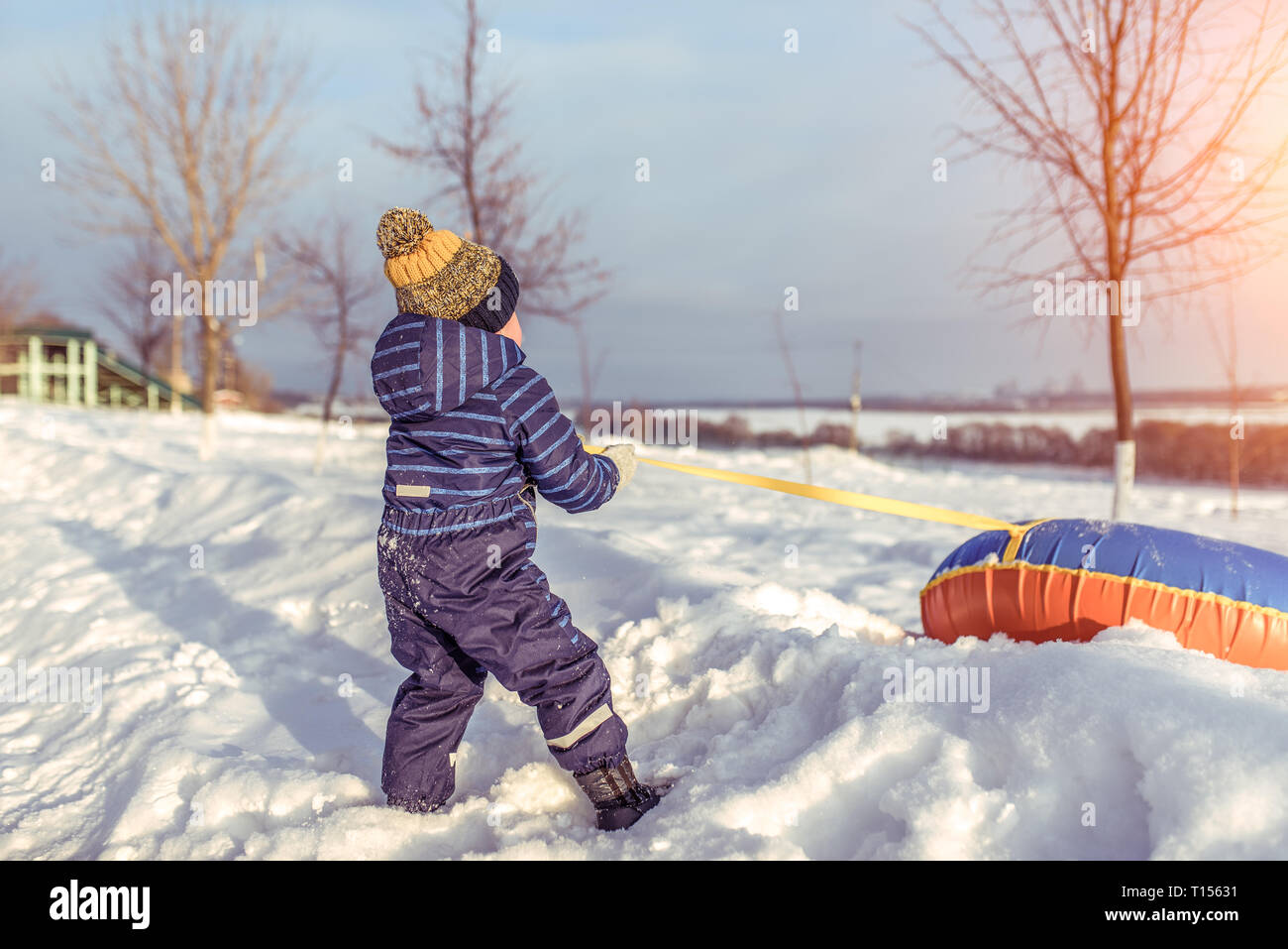 Ein kleiner Junge spielt im Winter draußen. Ziehen Sie ihr Spielzeug  Schlauch durch den Gurt, Seil, für die ein Abrollen der Folie. Rest am  Ferienort im Winter im Februar Stockfotografie - Alamy