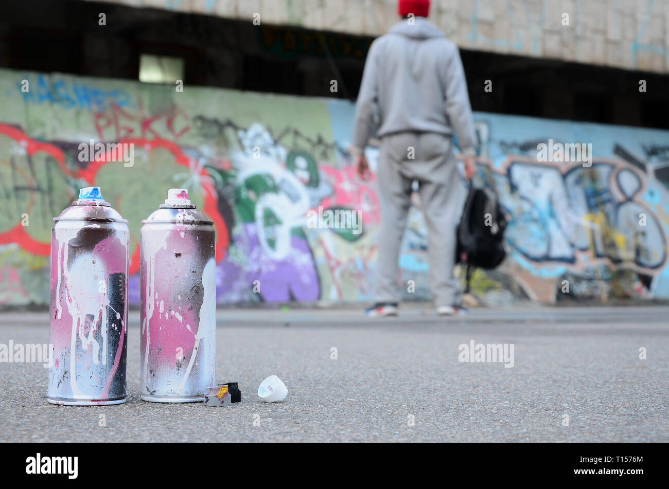 Mehrere verwendet, Spraydosen mit rosa und weisser Farbe auf den Asphalt gegen die ständigen Kerl vor einer bemalten Wand in farbigen Graffiti Zeichnungen Stockfoto