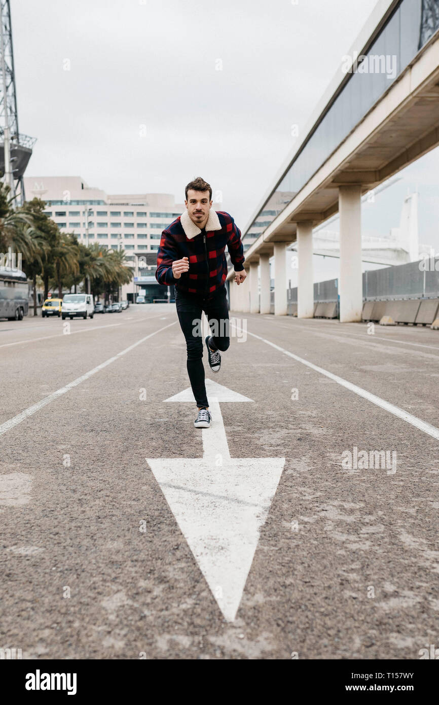Junger Mann mit legere Kleidung gelehnt auf dem Boden mit einem Fuß auf einen Pfeil auf den Boden gemalt Stockfoto