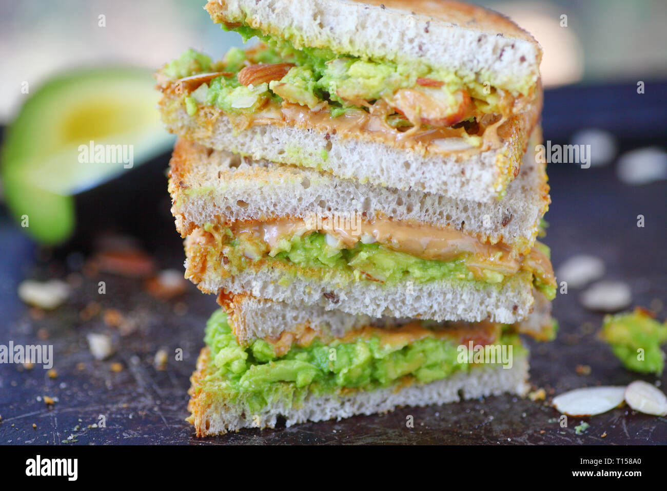 Gestapelte Drittel der ein Erdnussbutter und Guacamole Sandwich mit gehobelten Mandeln auf Roggen toast Stockfoto