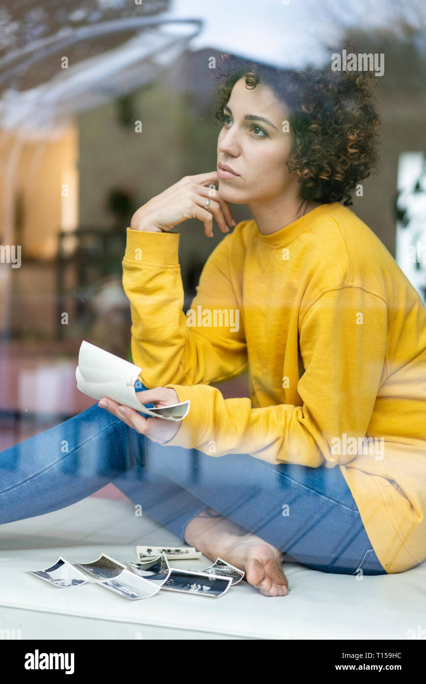 Ernsthafte Frau sitzt hinter dem Fenster zu Hause halten Fotos Stockfoto