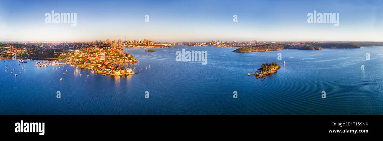 Wohlhabenden Vororten von Sydney am Ufer von Sydney Hafen mit Innenstadt hoch aufragenden Türmen und die Harbour Bridge am Horizont ist erhöht, Antenne weiten Schwenk Stockfoto