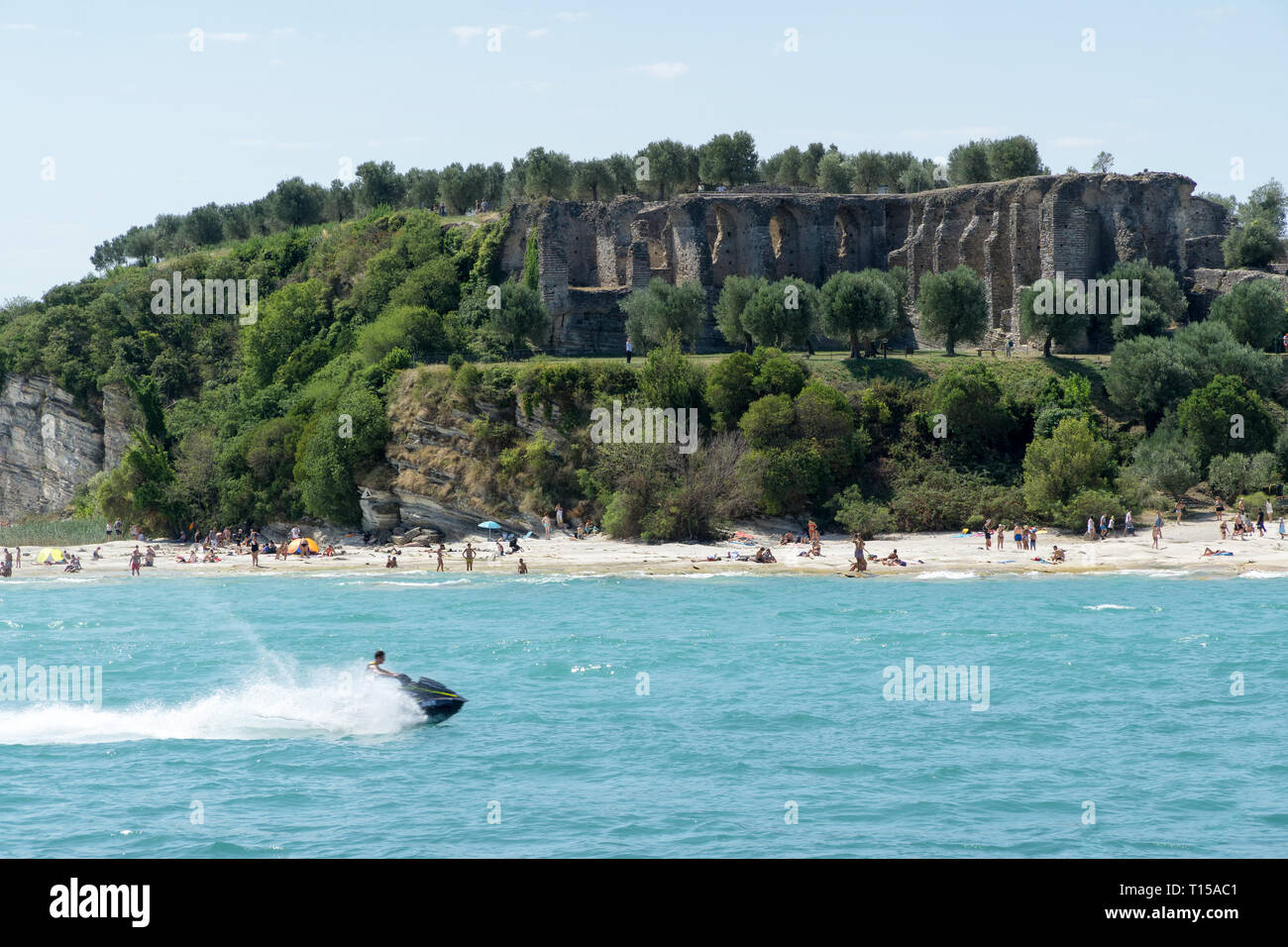 Steiniger Strand der Stadt Sirmione am Gardasee mit Blick auf die Grotten des Catull (Grotte di Catullo), die Ruinen einer römischen Villa am Ende der 1 Stockfoto