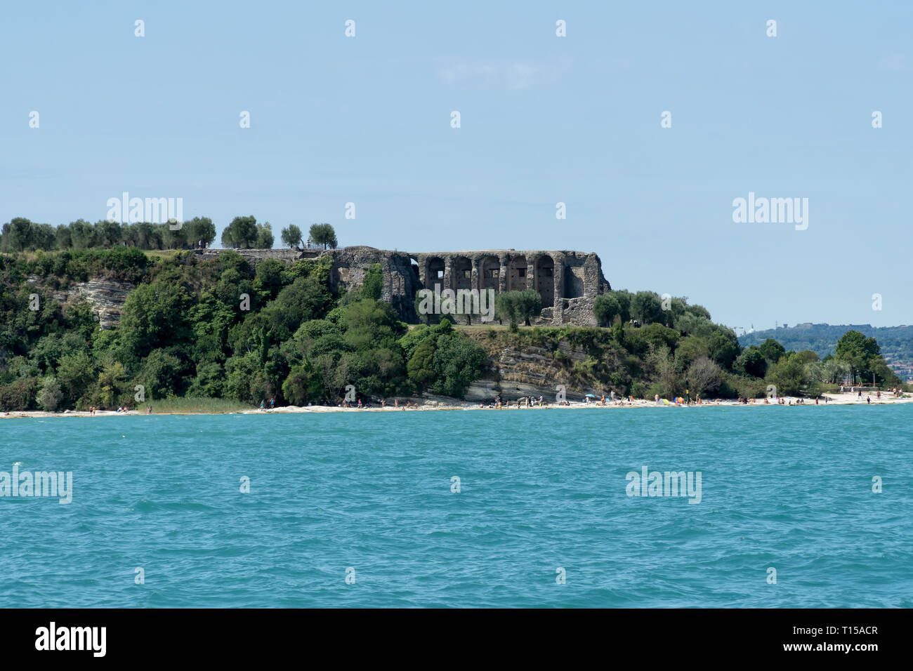 Steiniger Strand der Stadt Sirmione am Gardasee mit Blick auf die Grotten des Catull (Grotte di Catullo), die Ruinen einer römischen Villa am Ende der 1 Stockfoto