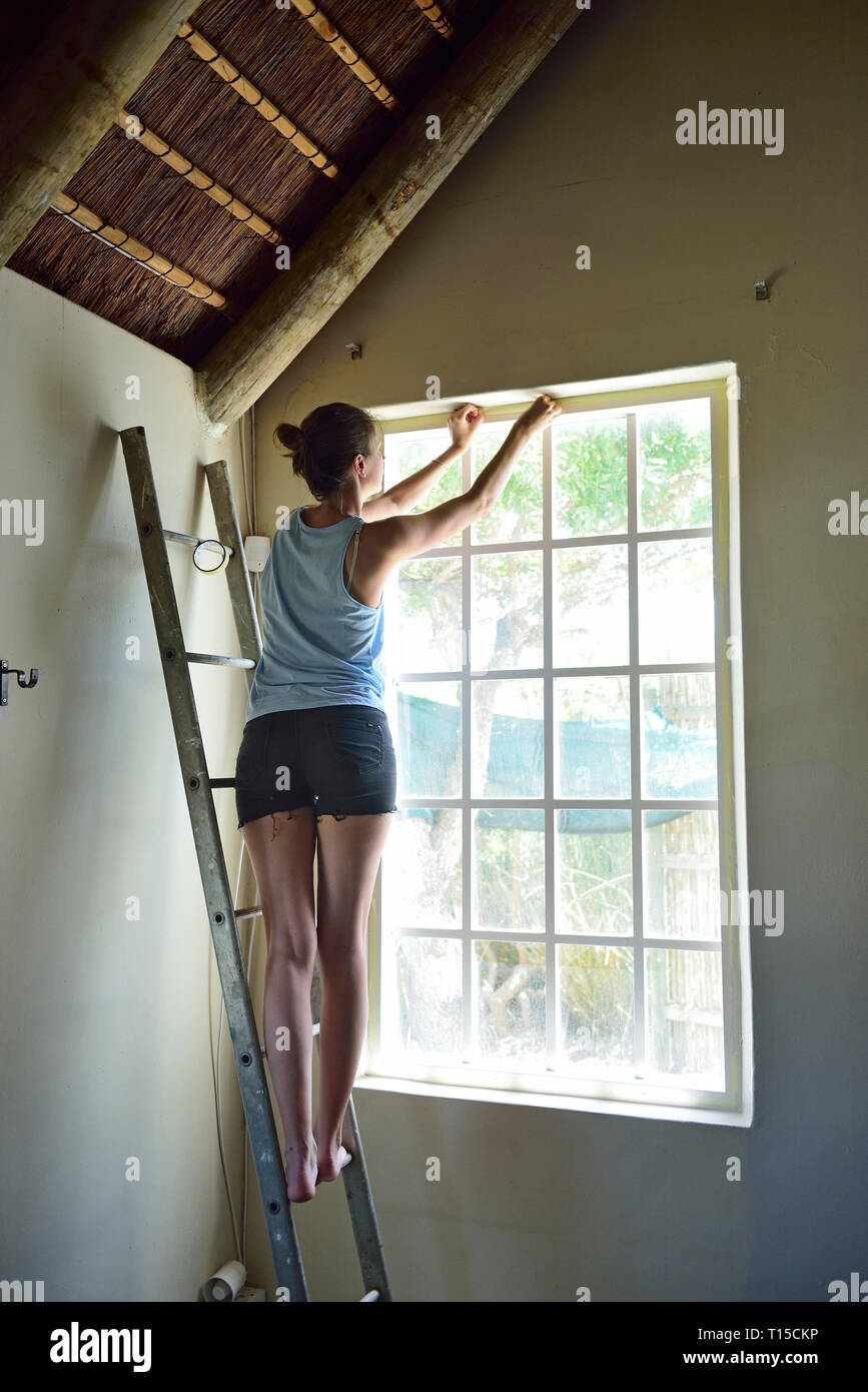 Junge Frau renovieren ihr Haus arbeiten bei Fensterrahmen Stockfoto