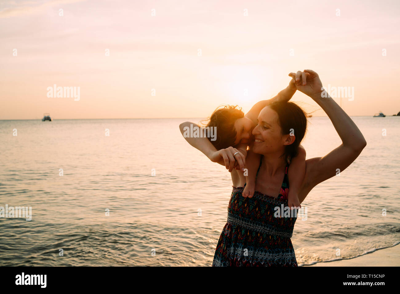 Thailand, Koh Lanta, glückliche Mutter mit Baby Mädchen auf ihren Schultern am Strand bei Sonnenuntergang Stockfoto
