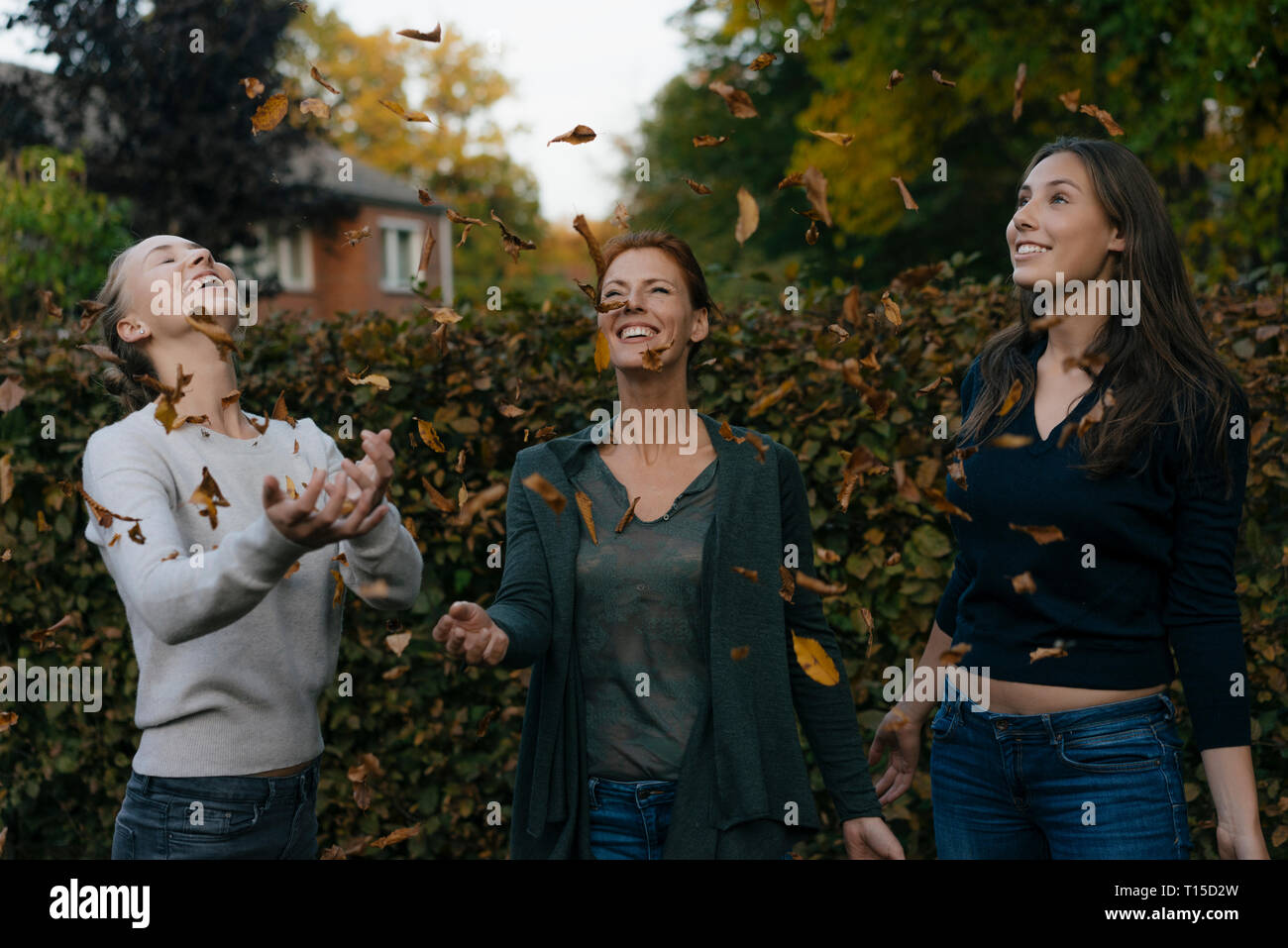 Sorglos Mutter mit zwei Töchtern im Teenageralter werfen Blätter im Herbst im Garten Stockfoto