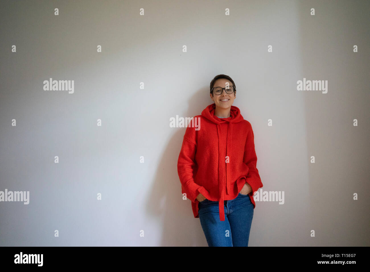 Porträt eines lächelnden jungen Frau mit kurzen Haaren, lehnte sich an der Wand Stockfoto