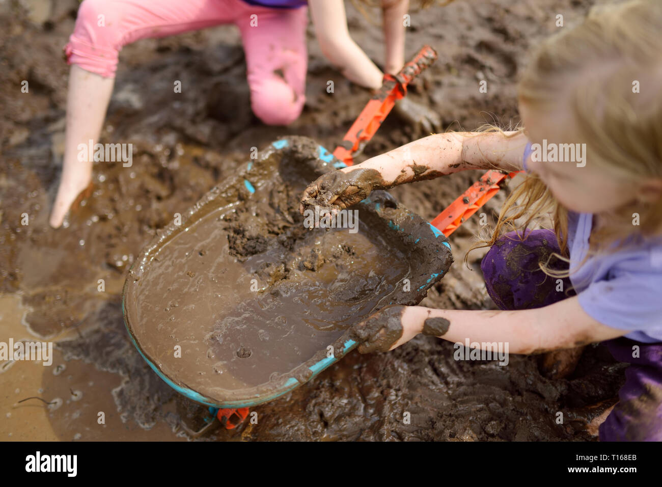 Zwei lustige kleine Mädchen, die in einem großen feuchten Schlamm Pfütze auf sonnigen Sommertag. Kinder Verschmutzung beim Graben in den schlammigen Boden. Unordentliche Spiele im Freien Stockfoto