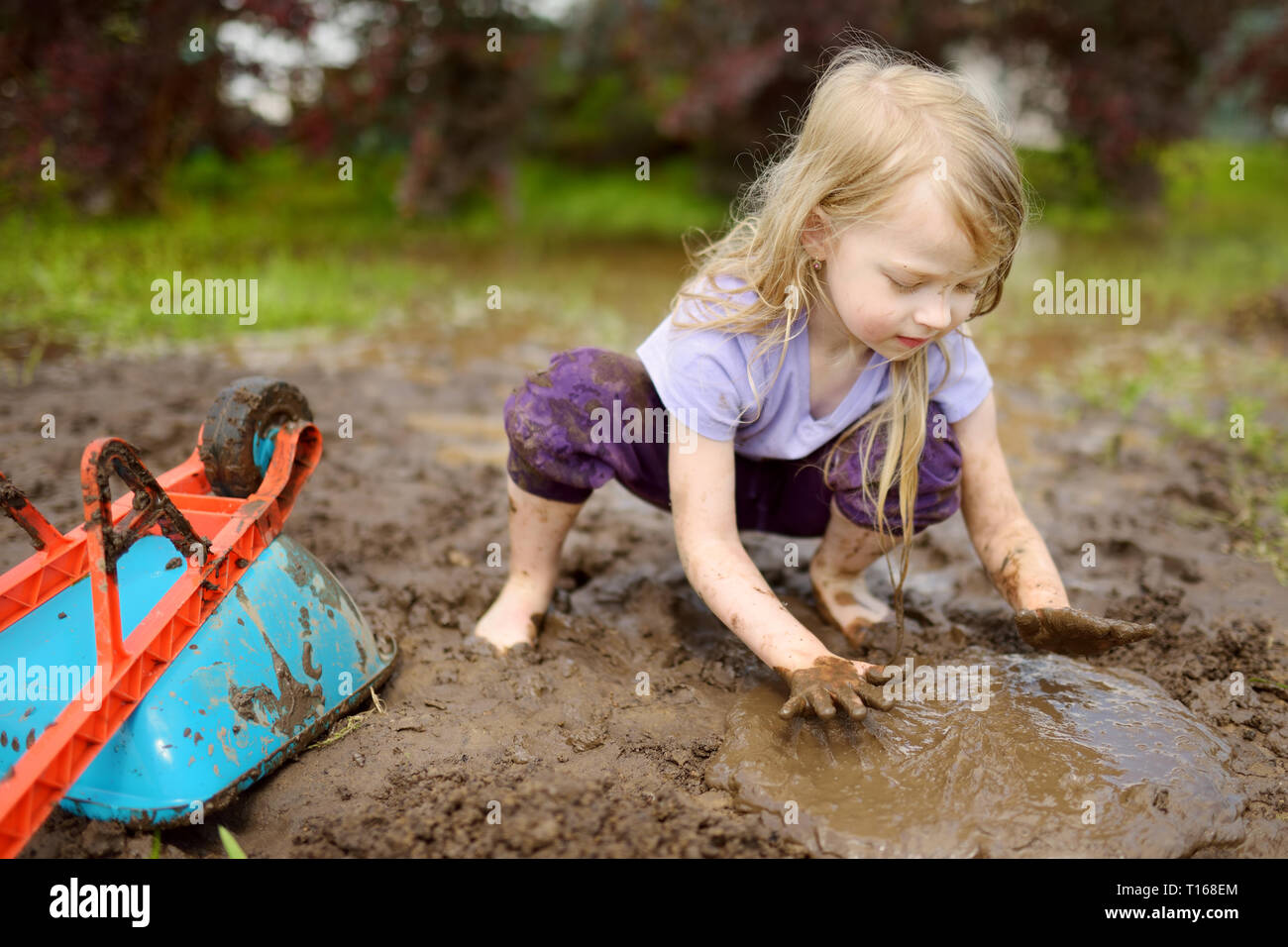 Lustige kleine Mädchen spielen in einem großen feuchten Schlamm Pfütze auf sonnigen Sommertag. Kind Verschmutzung beim Graben in den schlammigen Boden. Unordentliche Spiele im Freien. Stockfoto