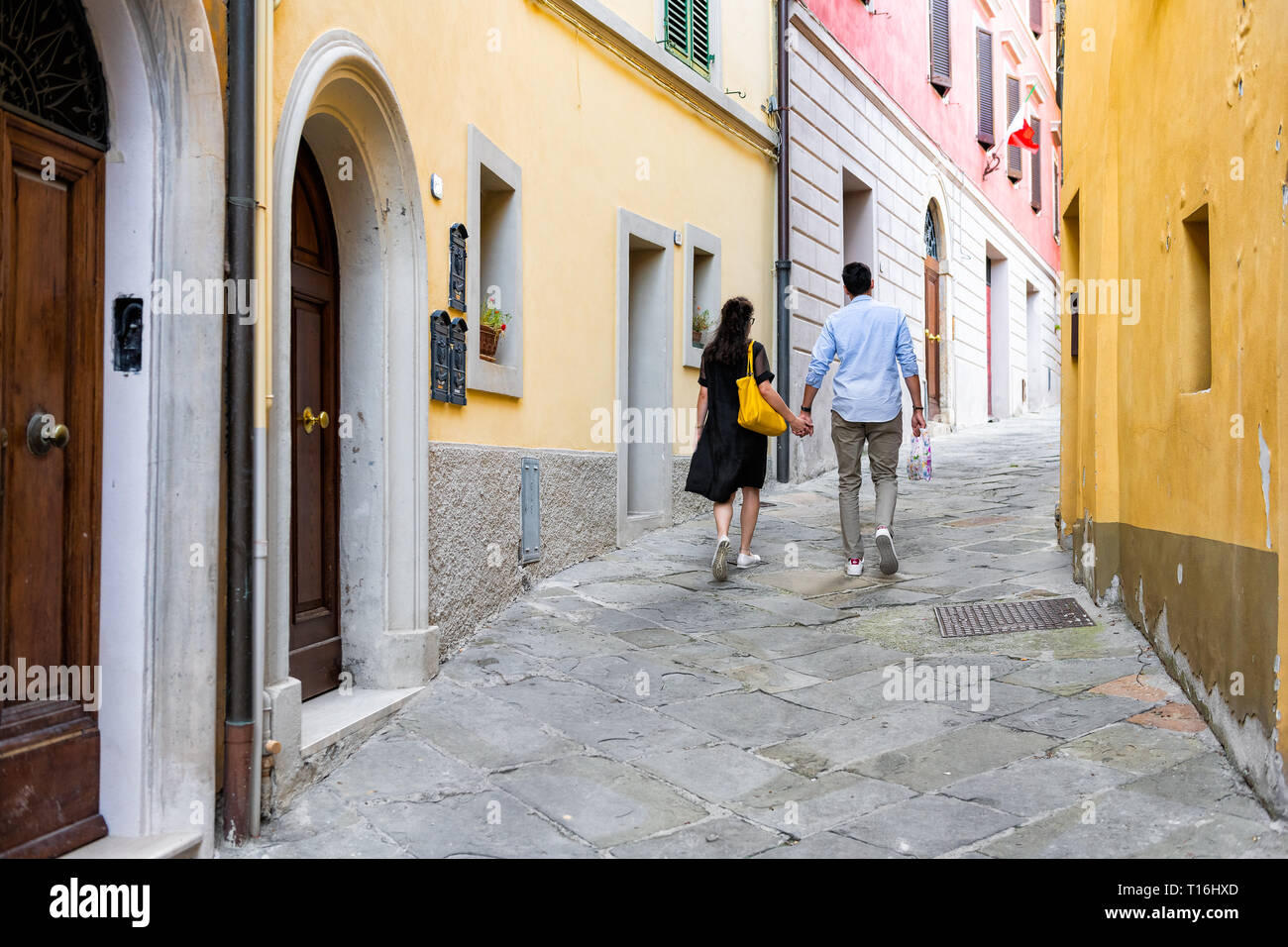 Chiusi, Italien - 25 August 2018: Alley street in kleinen Stadt Dorf in Umbrien Schmal bei Tag mit Leuten Paar hält Hände wandern durch orange Yel Stockfoto