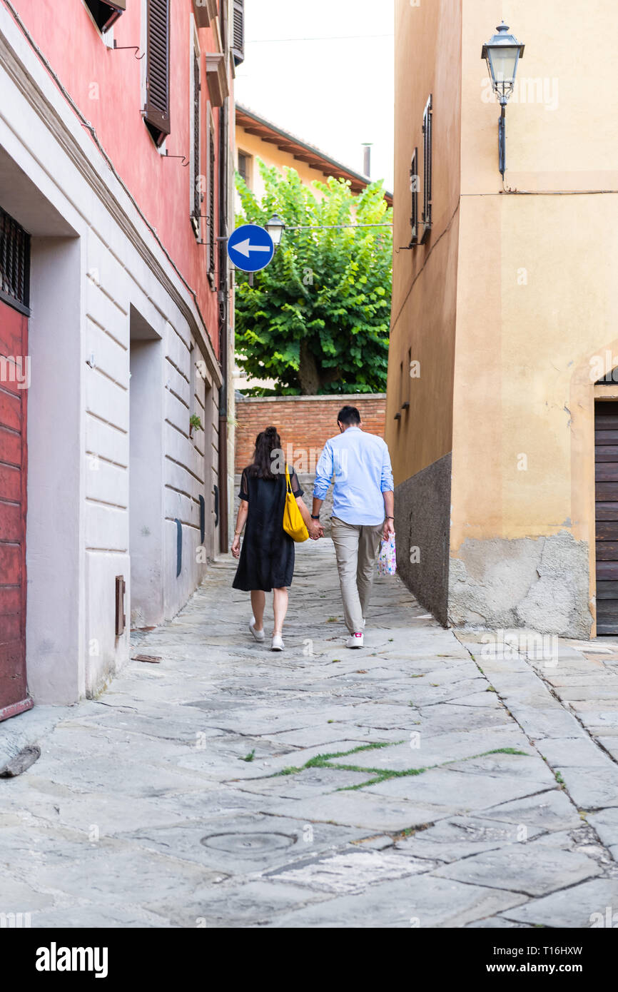 Chiusi, Italien - 25 August 2018: Alley street in kleinen Stadt Dorf in Umbrien bei Tag mit ein paar Hände halten zu Fuß durch orange gelb bunte Ein Stockfoto