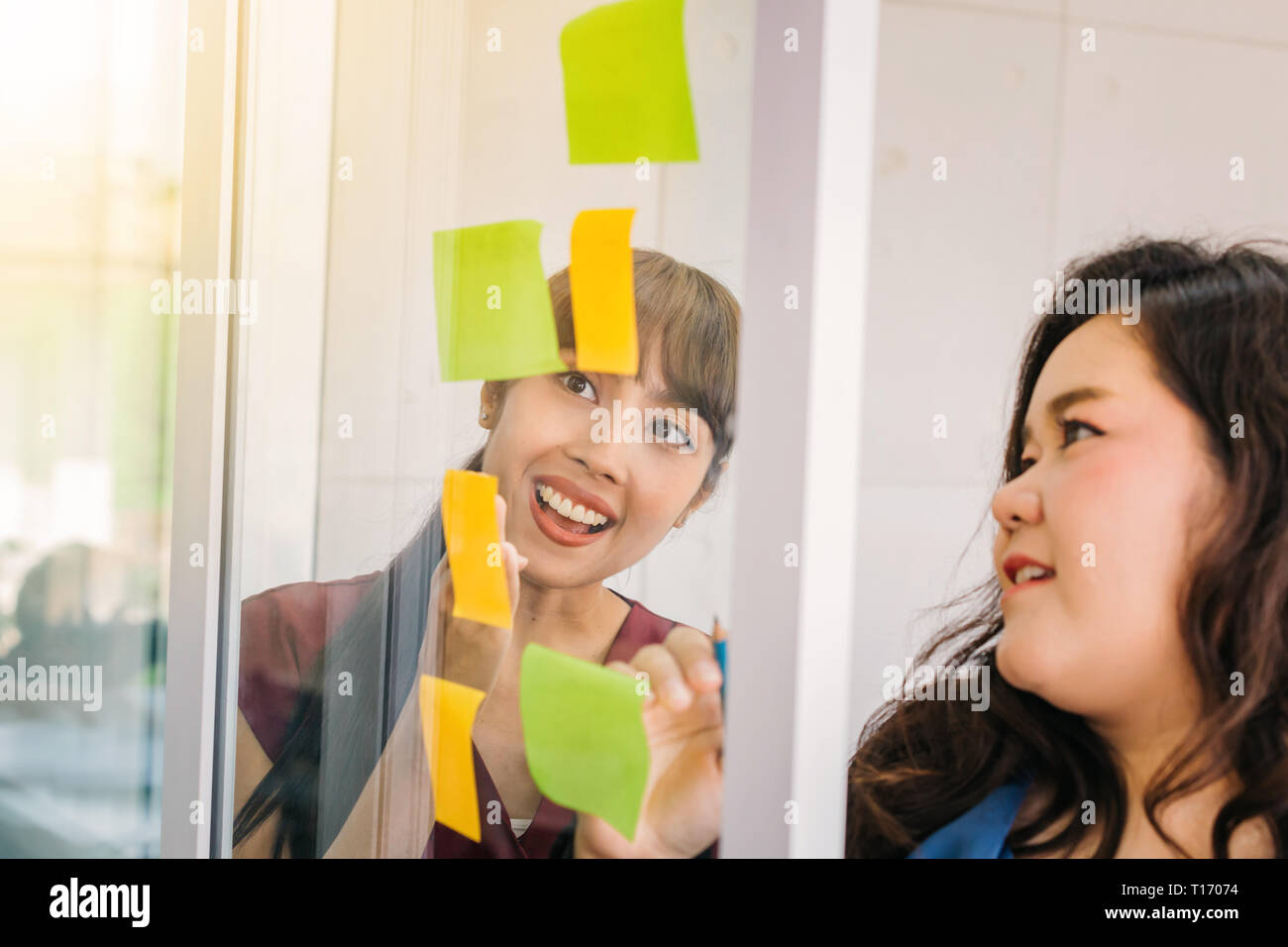 Asiatische glücklich Geschäftsfrauen diskutiert mit Haftnotizen auf Fenster im Büro Stockfoto