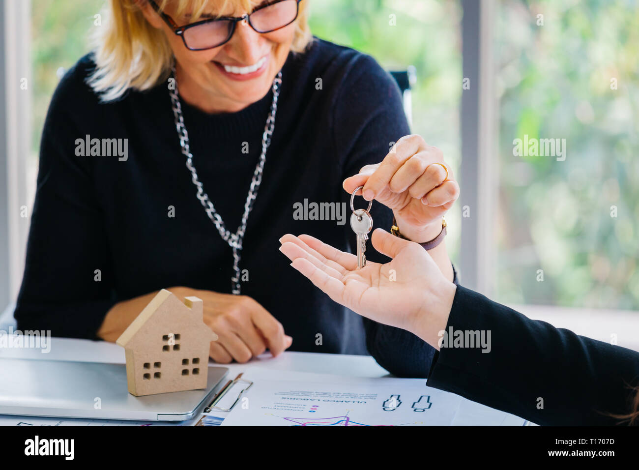 Nach Geschäftsfrau, Lächeln und die Taste Hand beim Sitzen am Schreibtisch mit Haus Modell im Büro von Immobilien Agentur zuschneiden Stockfoto