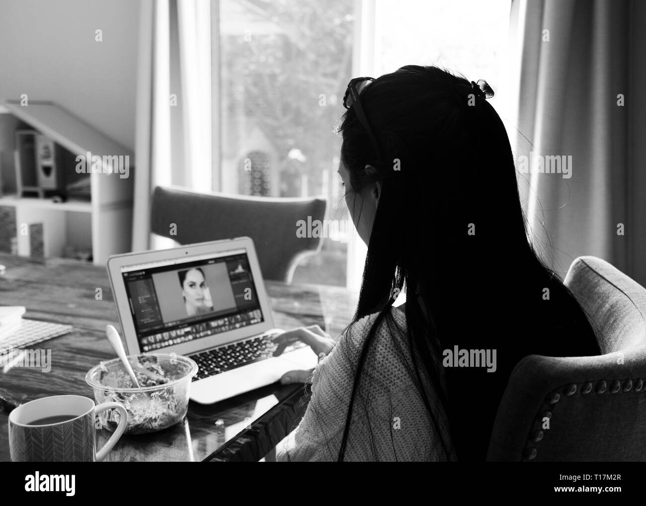 Junge Frau, die an einem Schreibtisch auf ihrem Laptop sitzt, mit Blick von der Seite in Schwarz und Weiß. Stockfoto