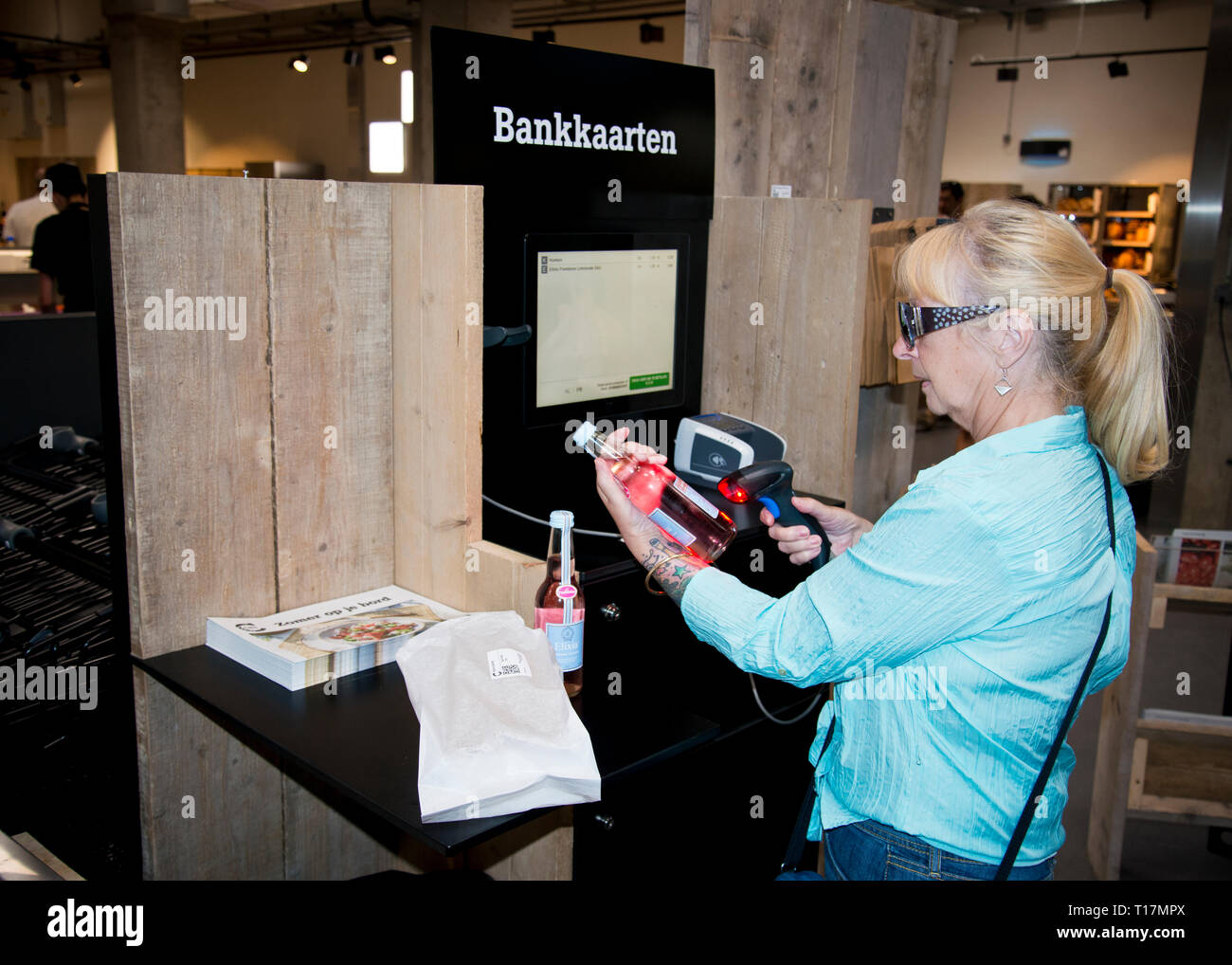 Frau mittleren Alters, die neue Technologie, Selbstscan für Shopping und Touchscreen-Technologie in einem Indoor-Stil Marktplatz umarmt.Gent, Belgien, Europa. Stockfoto