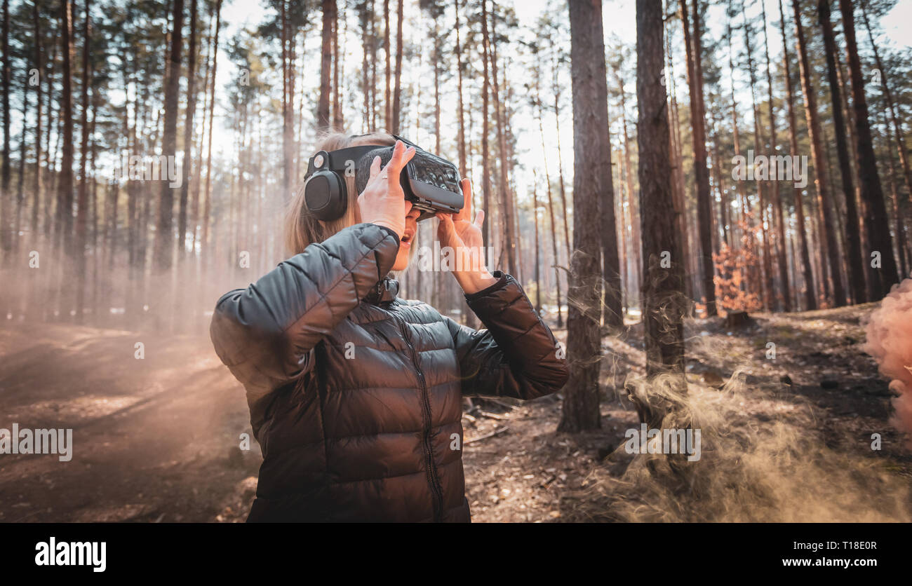 Frau im Wald mit Virtual reality Headset gerade Suchen mit orangen Rauch Rauchbomben Stockfoto