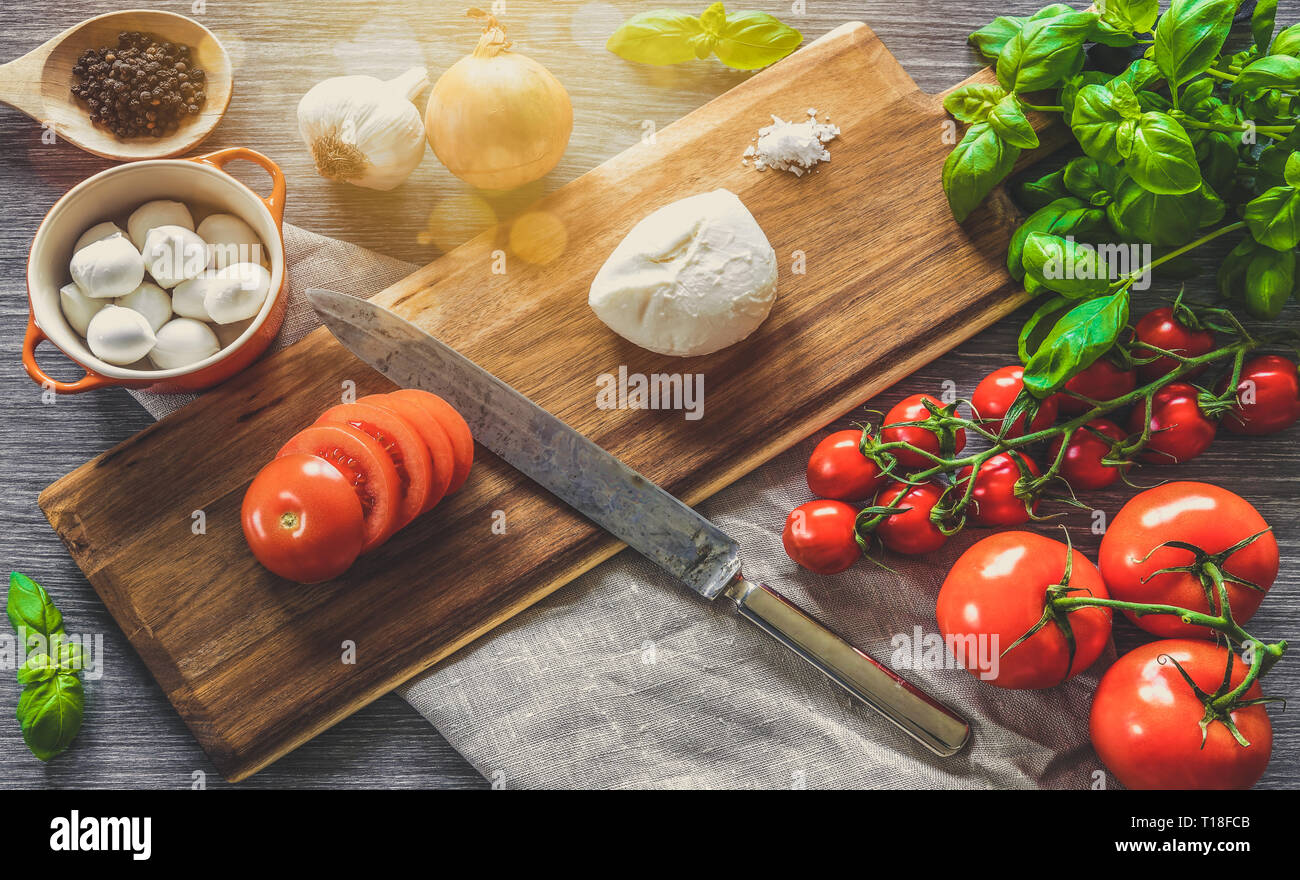 Italienisches Essen. Holz Schneidebrett von Zutaten zum Kochen, Gemüse und Mozzarella auf grauem Hintergrund umgeben. Stockfoto