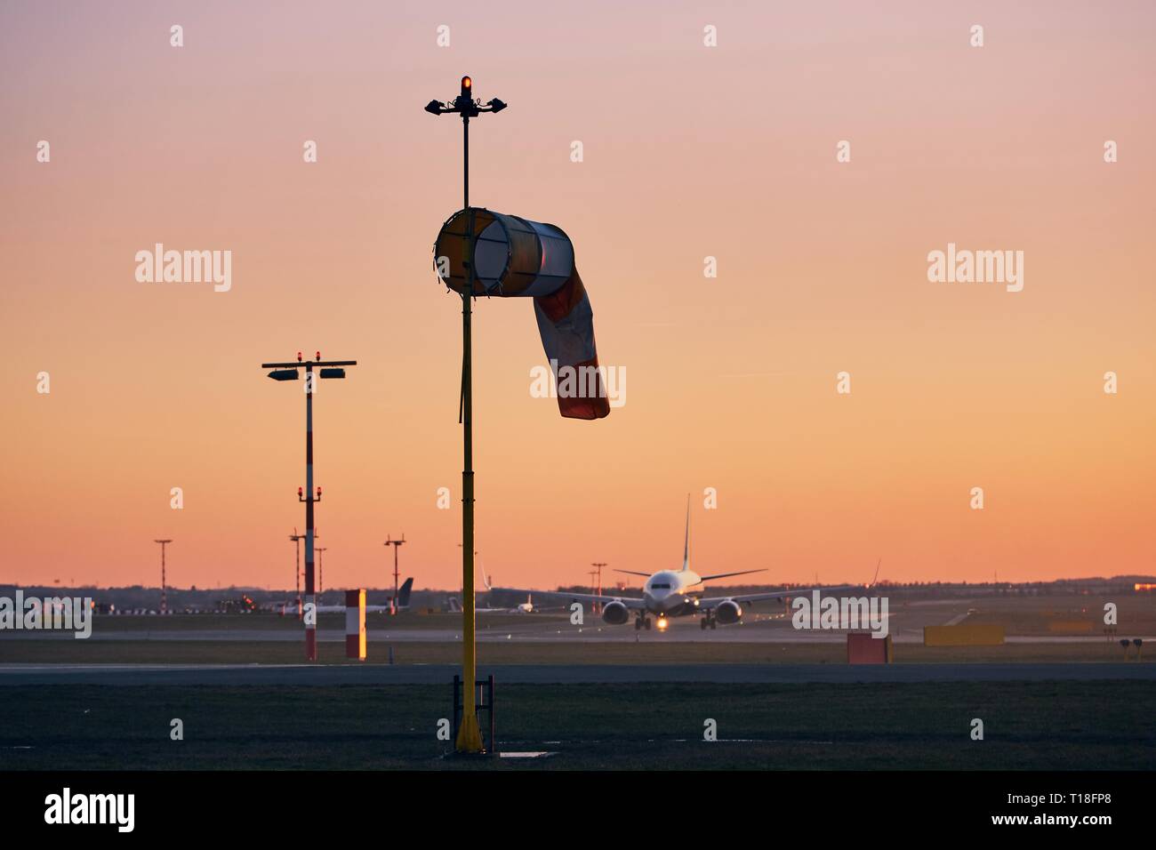 Gestreifte Windsack gegen Rollen Flugzeug. Flughafen bei Sonnenuntergang. Stockfoto