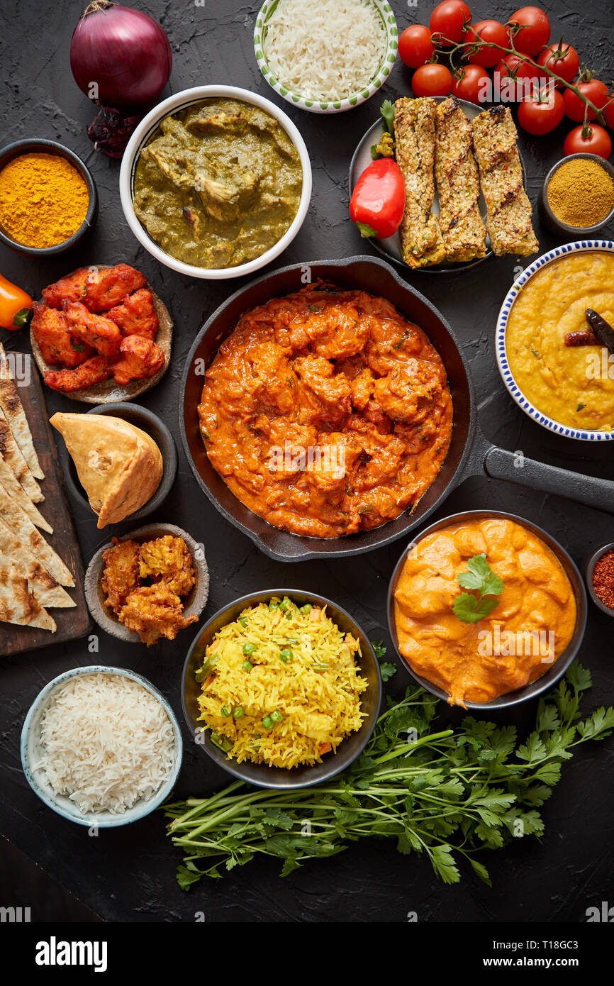 Verschiedene indische Gerichte auf dem Tisch. Spicy Chicken Tikka Masala in eiserne Pfanne. Mit Reis, Naan und Gewürzen serviert. Satz der anderen Art indisches Essen. Stockfoto