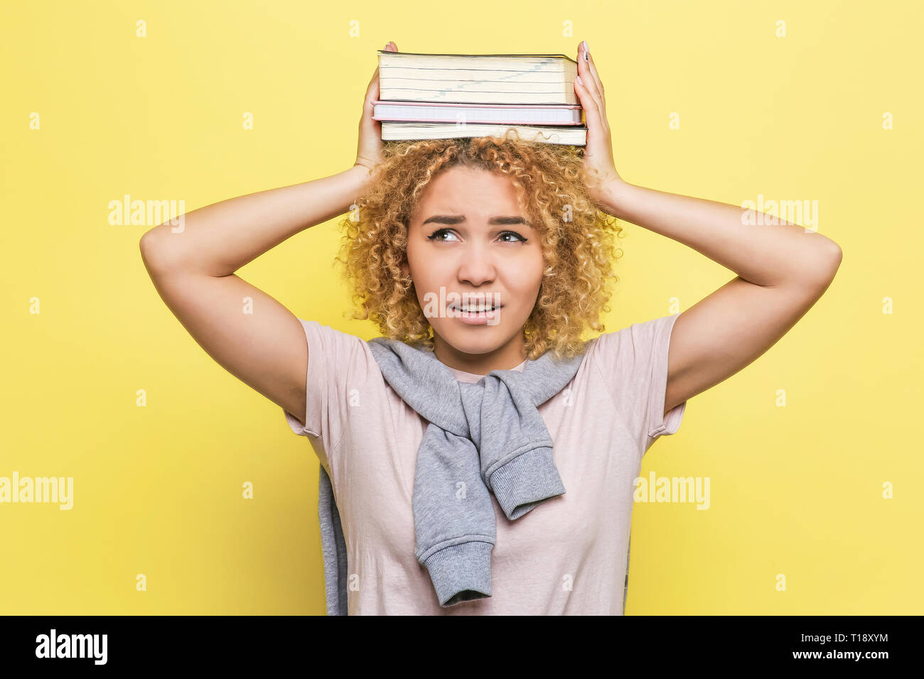 Unglücklich Studenten hält ein paar Bücher auf den Kopf. Sie hält Sie mit Ihren Händen. Mädchen nicht glücklich aus. Auf gelbem Hintergrund Stockfoto