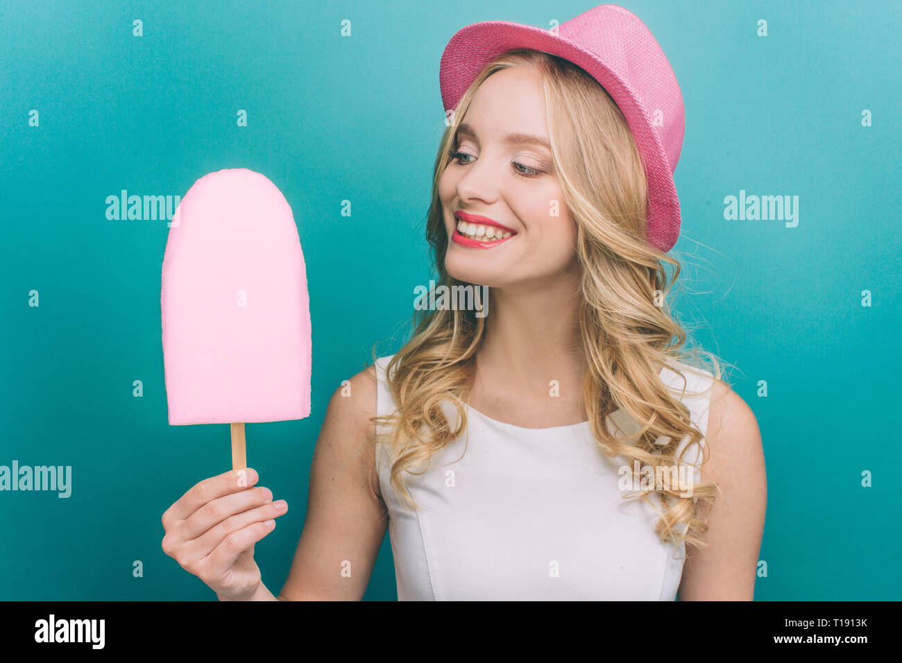 Schöne Mädchen hält ein großes rosa Eis. Sie schaut ihn an und lächelte. Mädchen möchte, es zu essen. Auf blauem Hintergrund isoliert Stockfoto