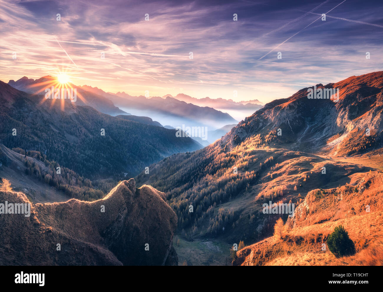 Berge im Nebel bei Sonnenuntergang im Herbst. Dolomiten, Italien. Landschaft mit Alpine Mountain Valley, orange Gras, Wolken, Bäume auf Hügeln, pur Stockfoto