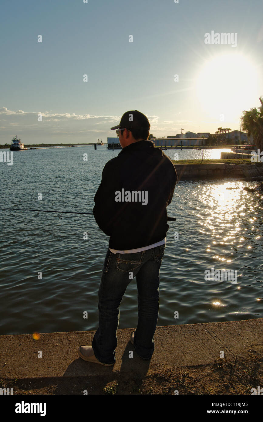 Junger Mann angeln auf einem Zement Pier bei Sonnenuntergang Stockfoto