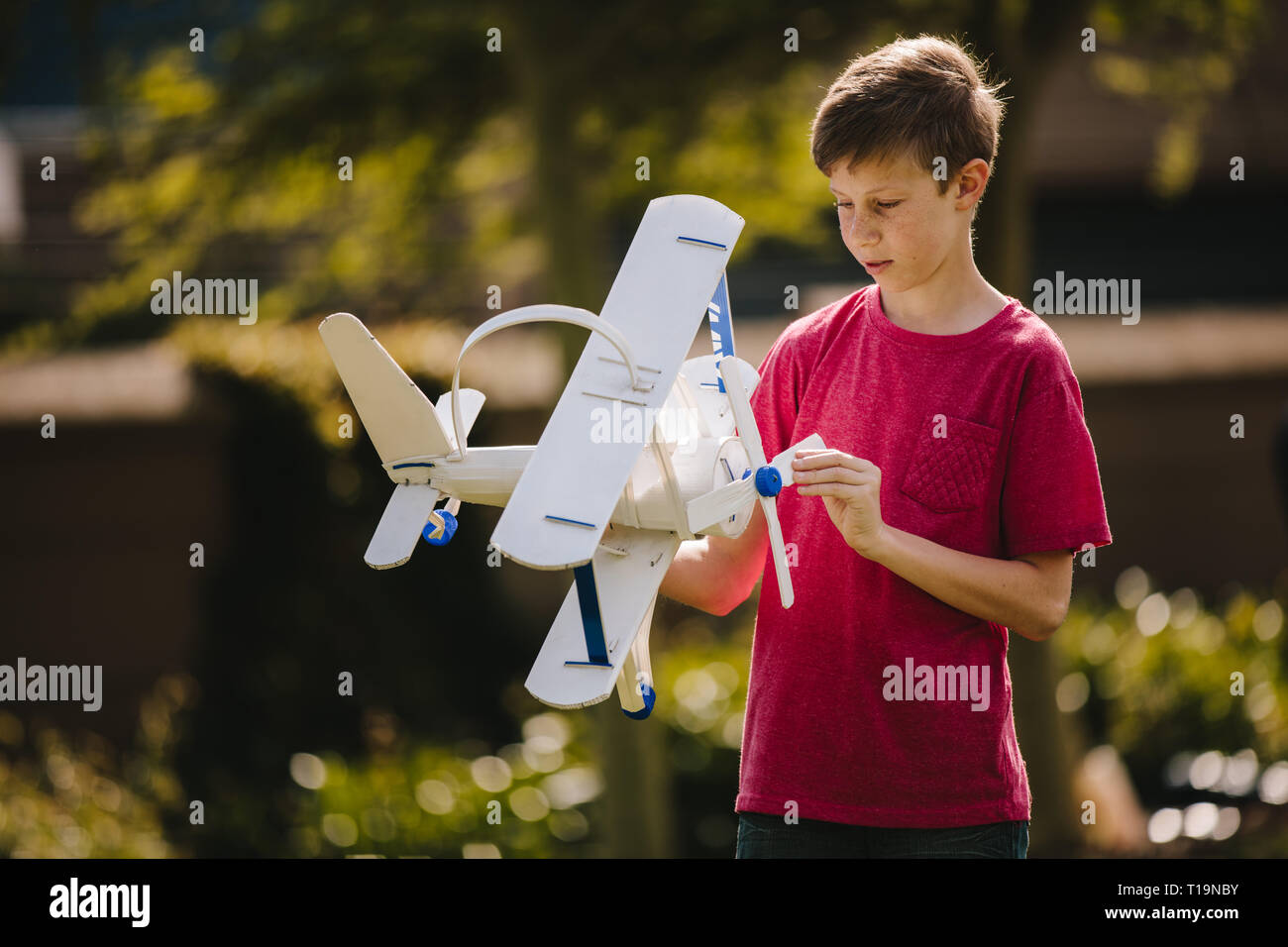 Junge spielt mit einem Spielzeug Flugzeug im Freien. Jugendliche junge Blick auf das Spielzeug Flugzeug in seine Hände im Freien. Stockfoto