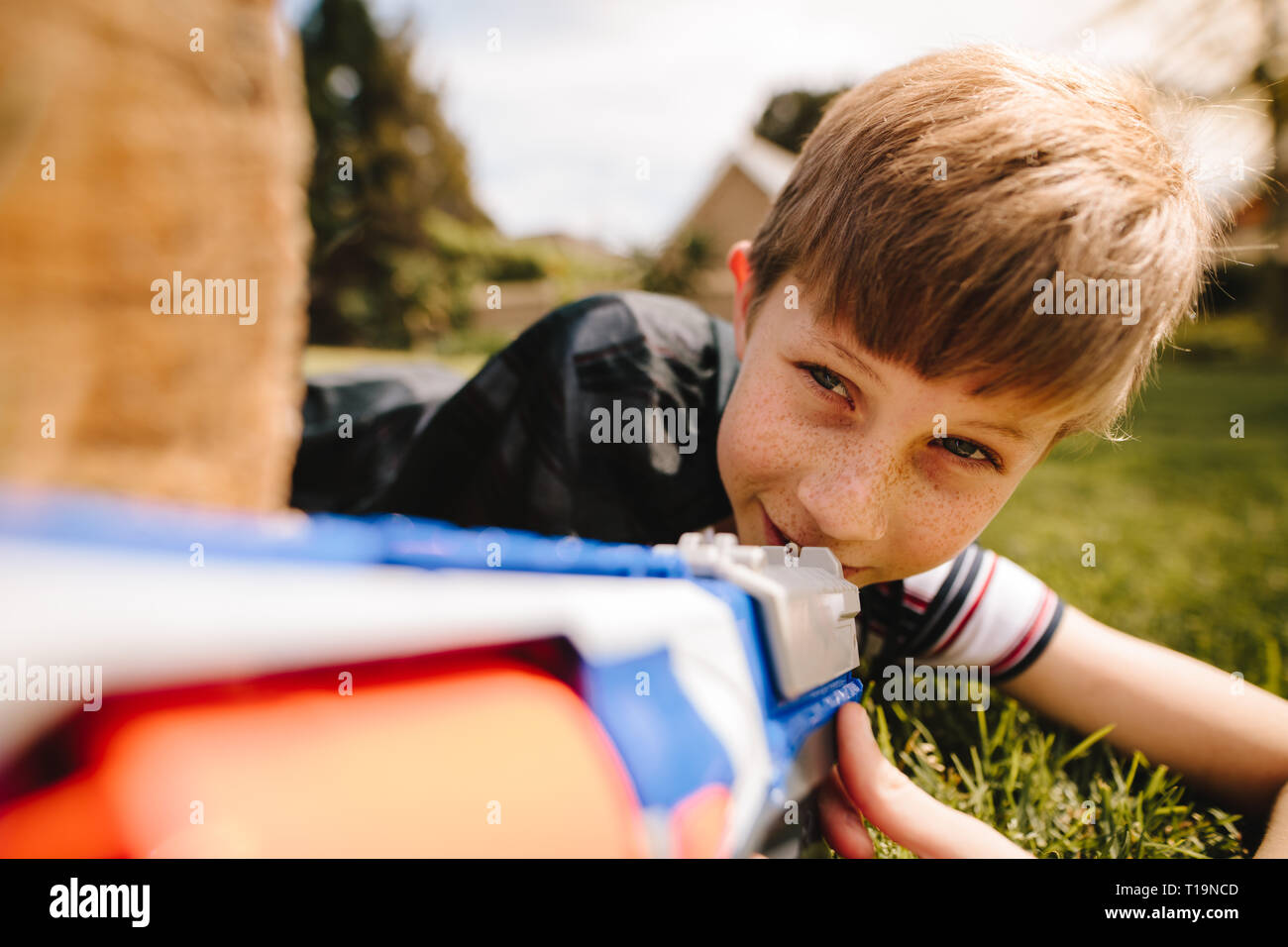 Kid in Kap versteckt sich hinter einem hölzernen mit spielzeugpistole in der Hand anmelden. Cute Boy spielen mit Spielzeug gewehr im Spielplatz. Stockfoto