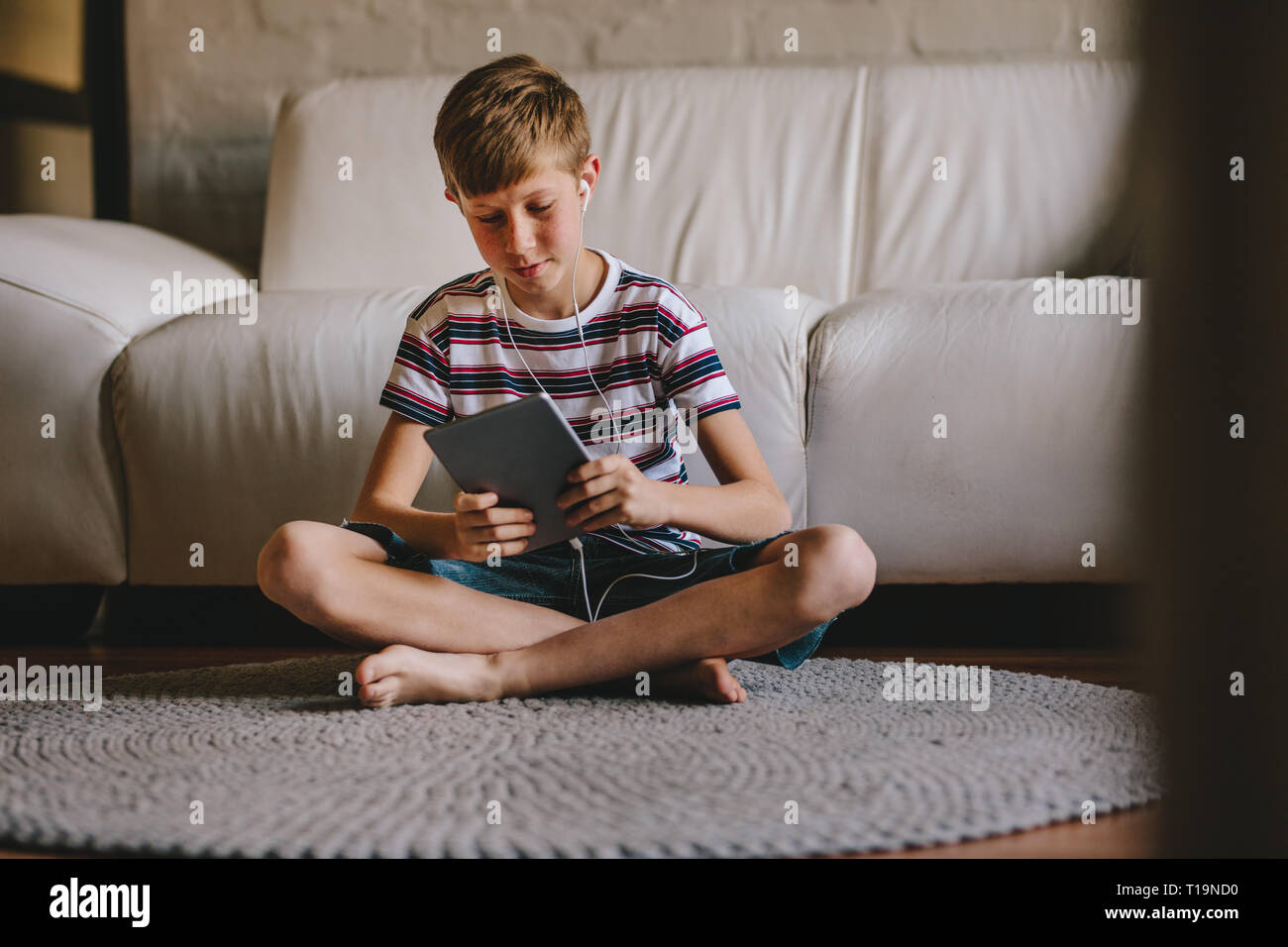 Junge Junge sitzt auf dem Boden tragen Kopfhörer und Videospiele auf digital Tablet. Junge in Kopfhörer spielen online Spiel auf Tablet-PC zu Hause. Stockfoto