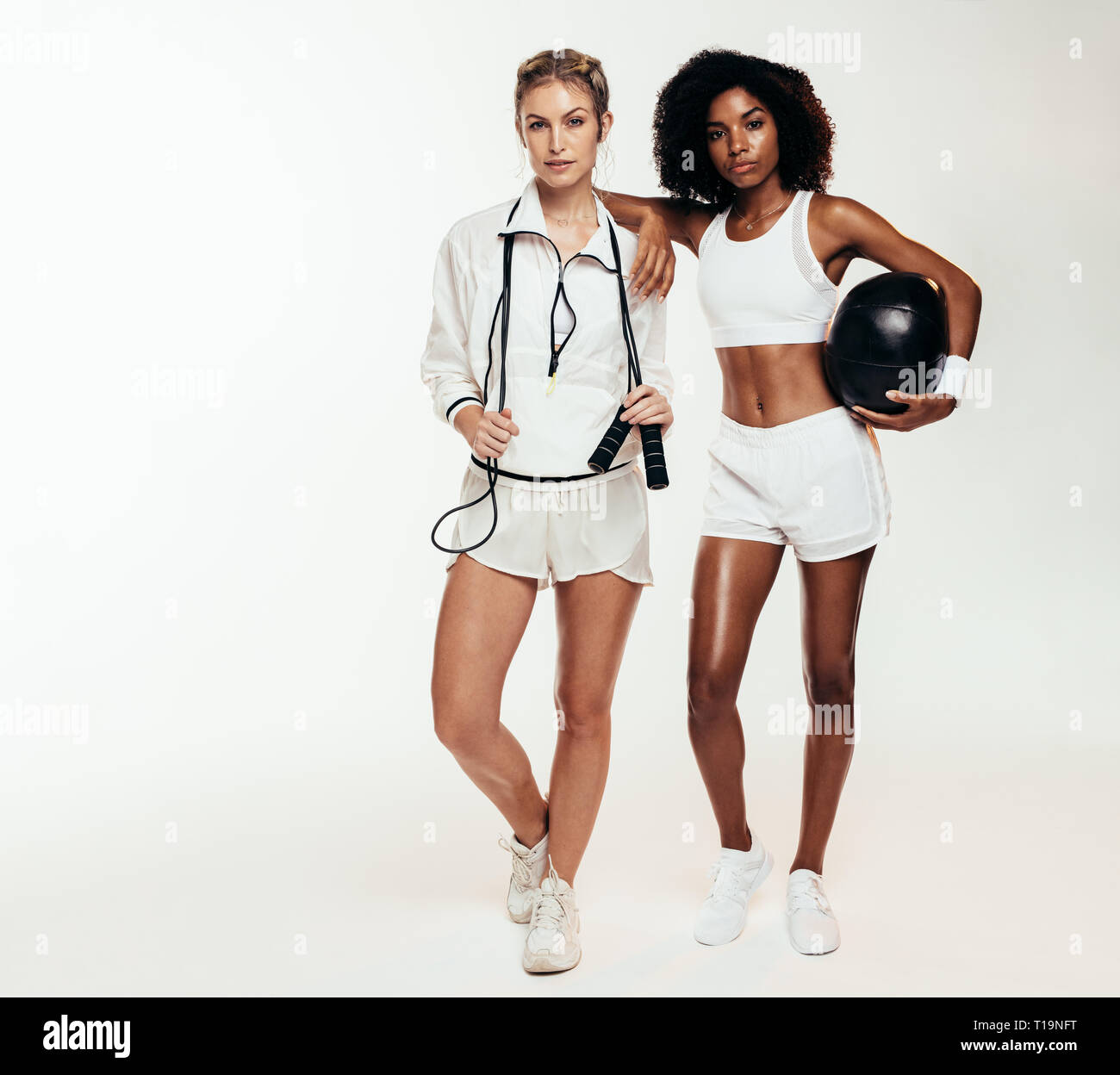 Die volle Länge der Frauen in Sportkleidung gemeinsam mit Medizin ball und Springseil. Zwei Frauen mit Sportgeräte stehen über weiße Hinterg Stockfoto