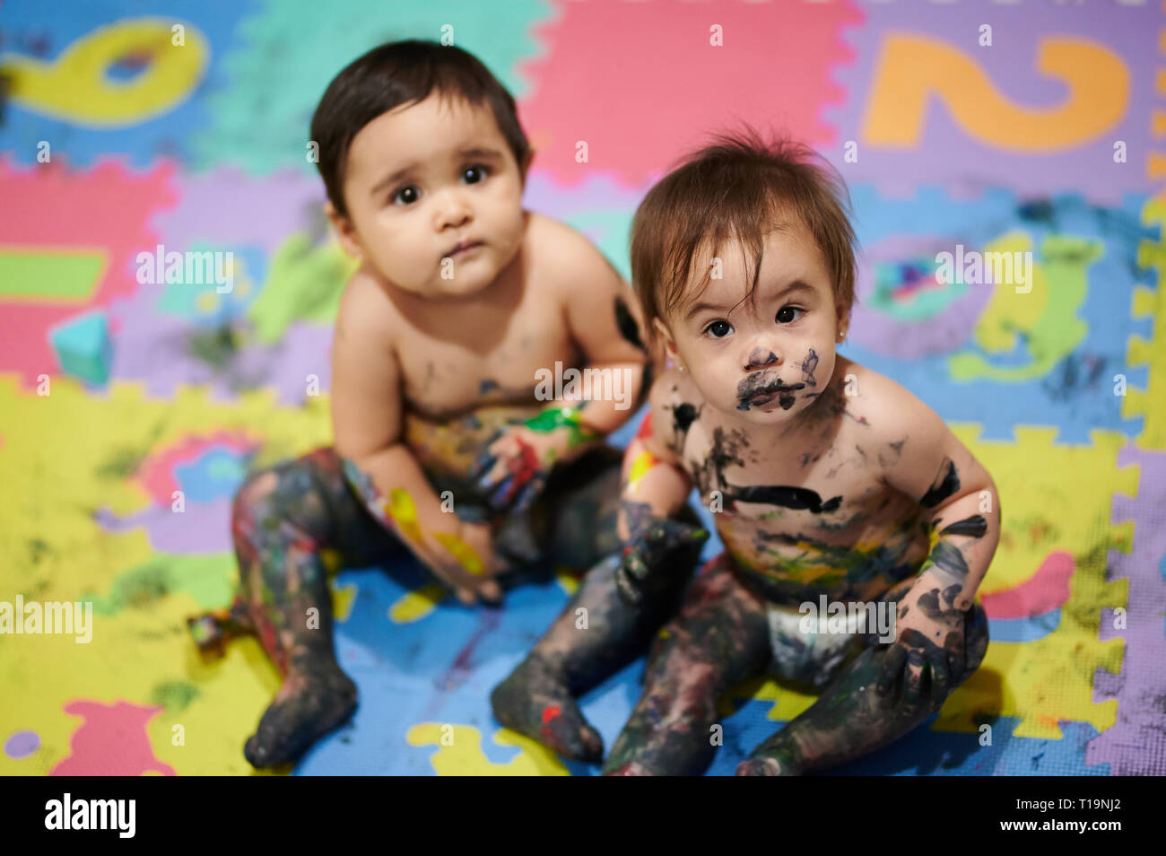 Bemalte Kinder sitzen auf bunten Hintergrund. Babys machen Chaos Stockfoto