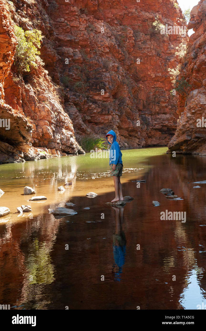 Ein kleiner Junge spielt auf dem Sprungbrett in die Untiefen der Simpsons Gap, Northern Territory, Australien Stockfoto