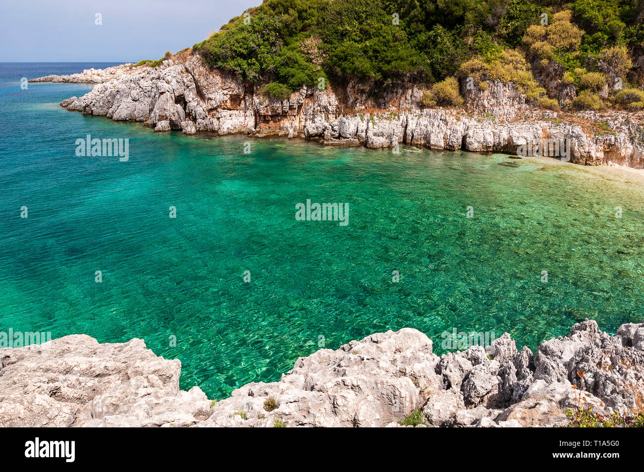 Eine kleine Bucht mit blauen, kristallklaren Wasser aus dem griechischen Meer. Landschaft beim Wandern, der felsigen Küste mit mediterranen Pflanzen und turqo gesehen Stockfoto